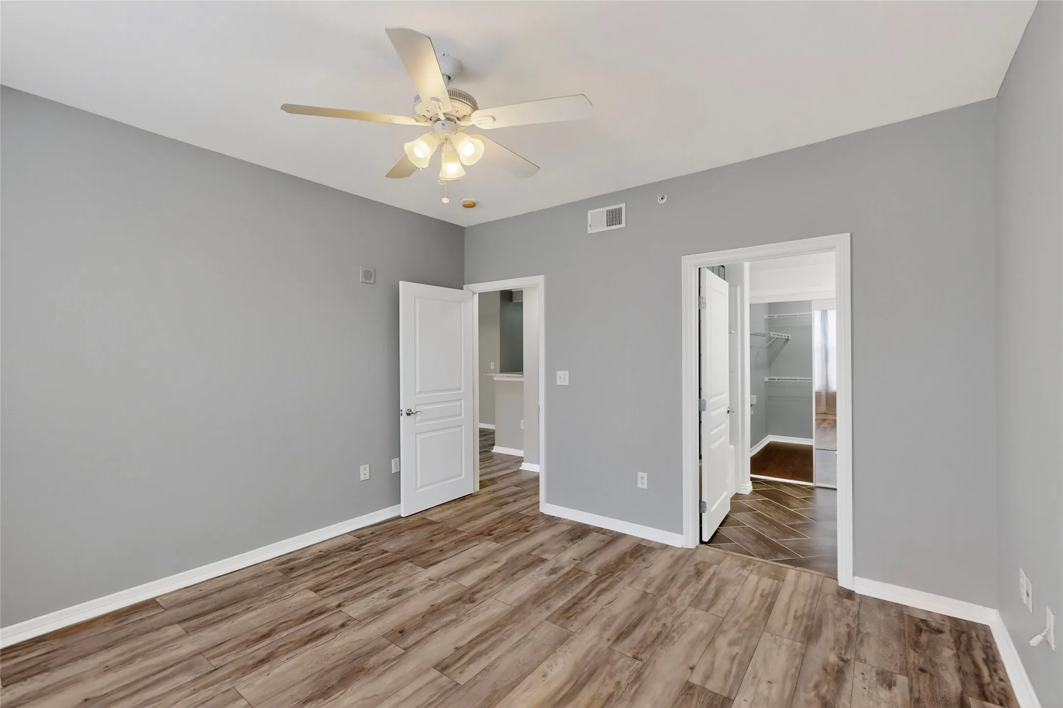 Unfurnished bedroom with wood finished floors, a ceiling fan, and a walk in closet