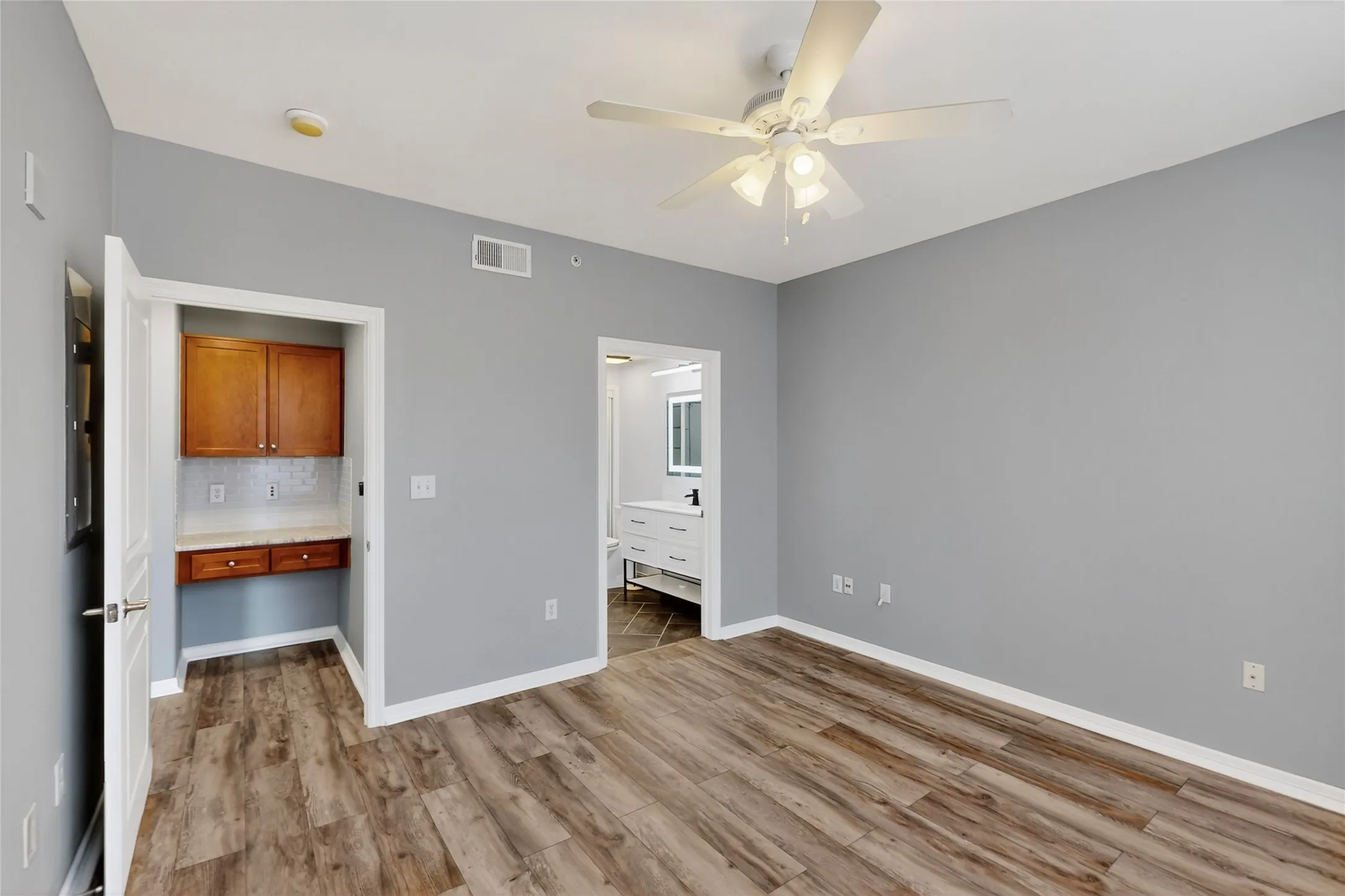 Unfurnished bedroom with light wood-type flooring, ensuite bath, and ceiling fan