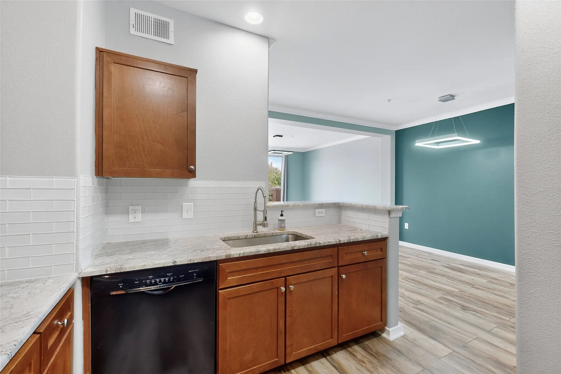 Kitchen featuring black dishwasher, tasteful backsplash, brown cabinetry, light wood-style flooring, and crown molding