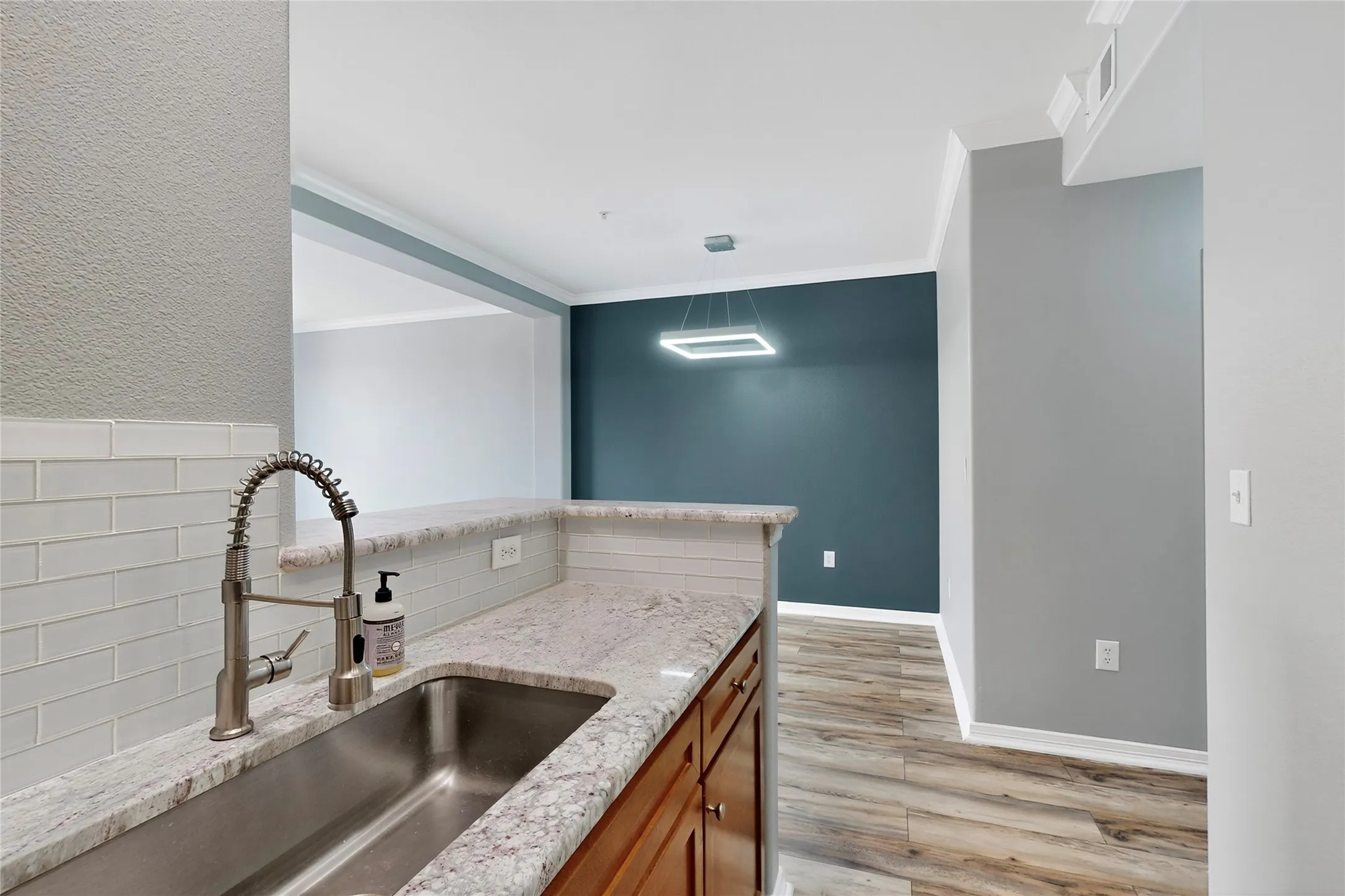 Kitchen featuring brown cabinets, ornamental molding, light wood-type flooring, light stone counters, and decorative backsplash