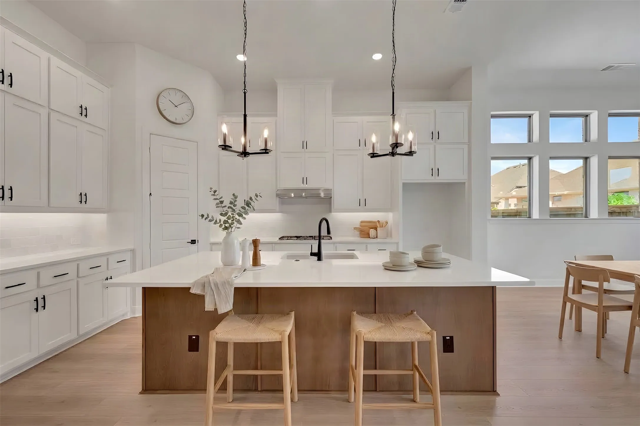 White shaker cabinetry with matte black hardware, a large kitchen island with a white countertop, stainless steel appliances, wood-finish flooring, and multi-pane windows
