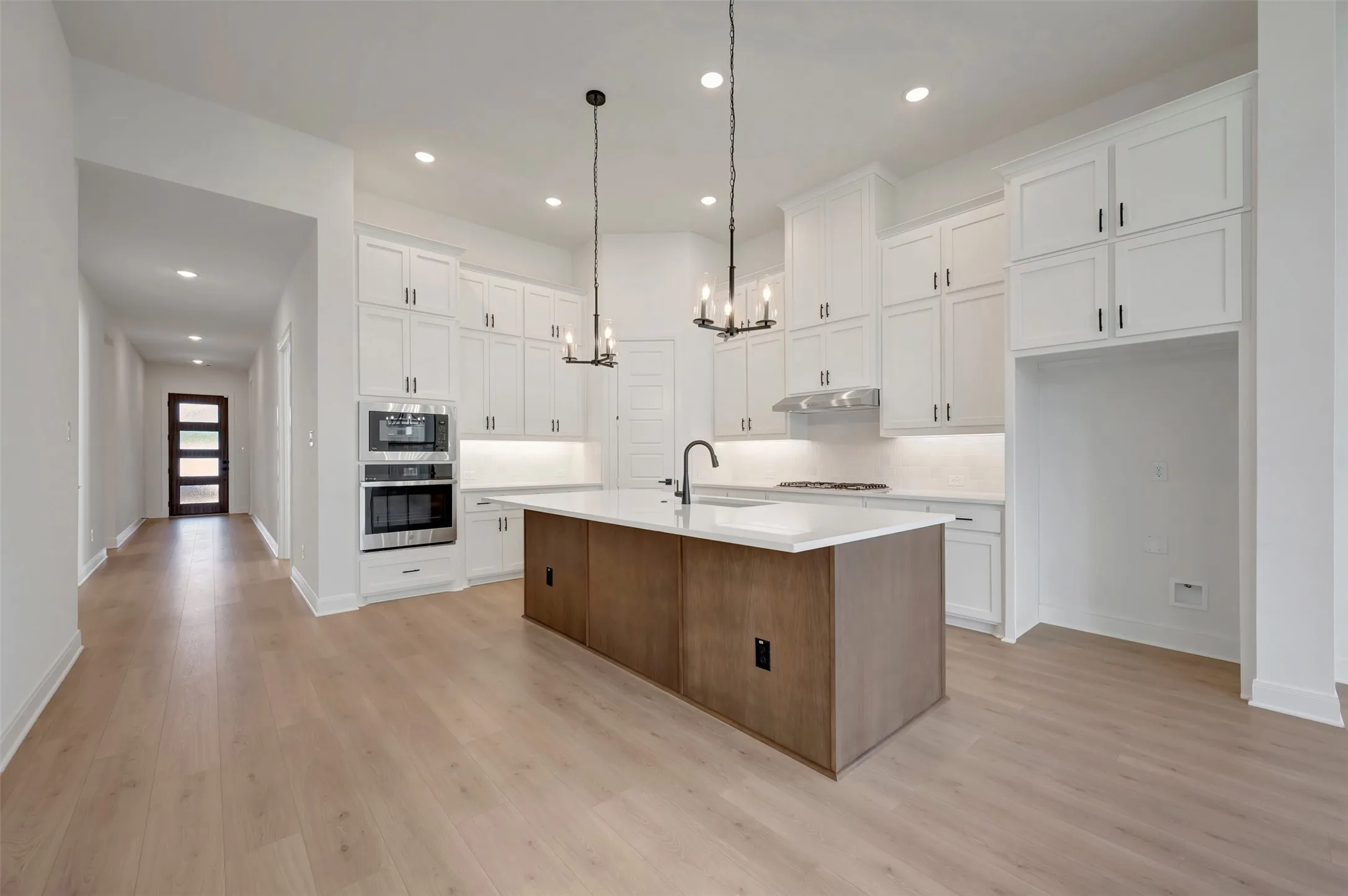Spacious kitchen with wood-finish flooring, white cabinetry, a built-in oven and microwave, and a large central island with a sink