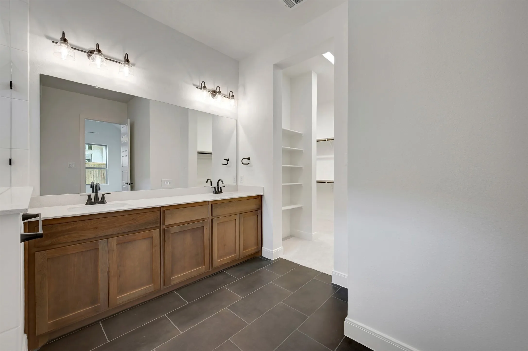 Dual vanity with wood-finish cabinetry, light-toned countertop, rectangular undermount sinks, and dark-toned tile flooring