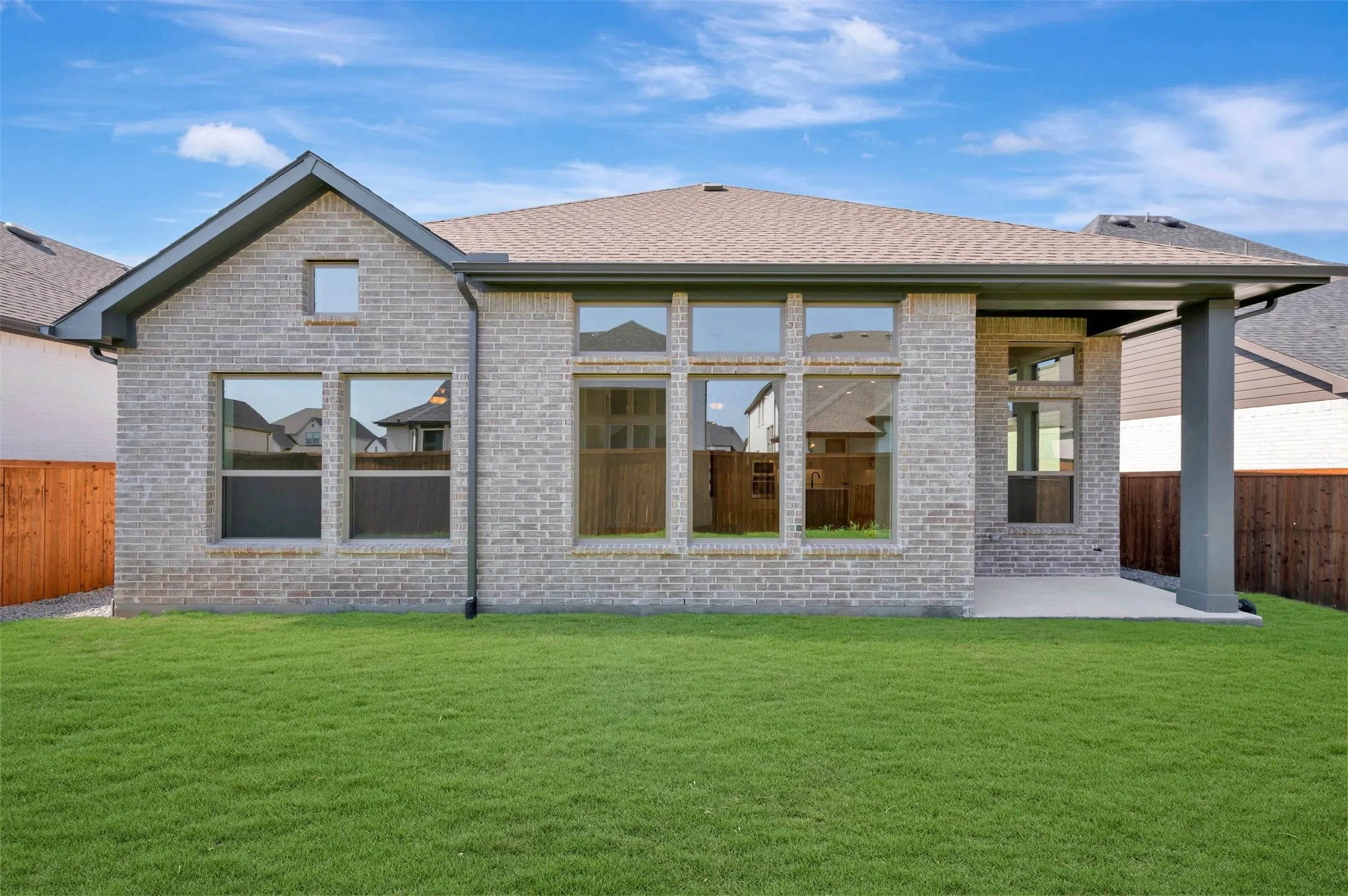 Brick exterior with multiple windows, covered patio, and a shingled roof