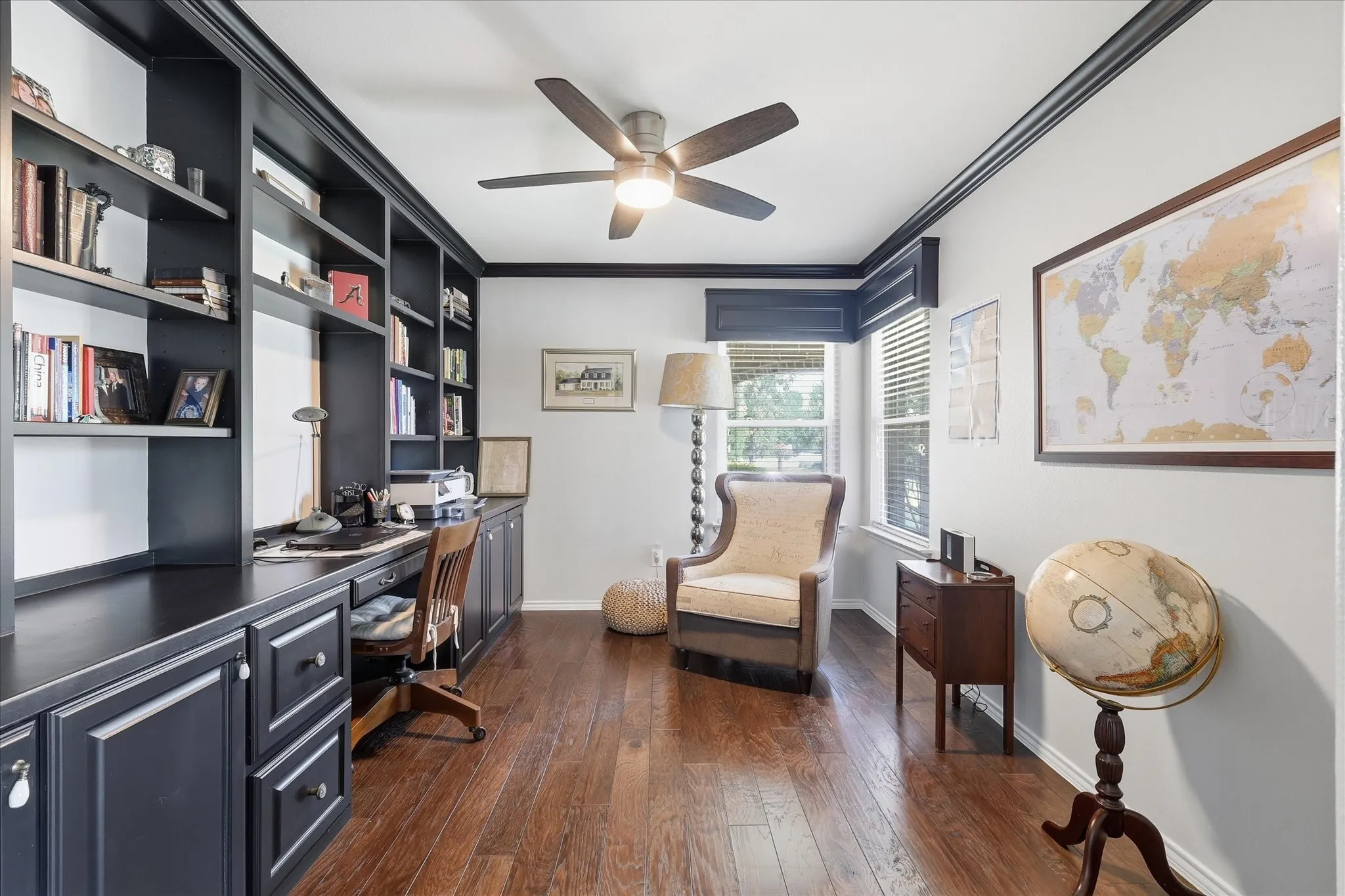 Dedicated office space featuring extensive built-in cabinetry and shelving, dark wood-finish flooring, dark crown molding, and a ceiling fan with integrated lighting