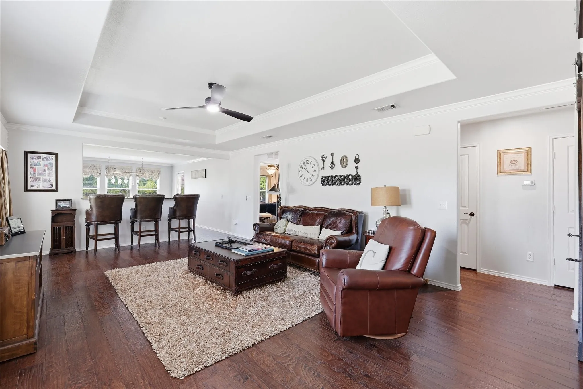 Spacious living area featuring rich wood-finish flooring, a tray ceiling, and a contemporary ceiling fan
