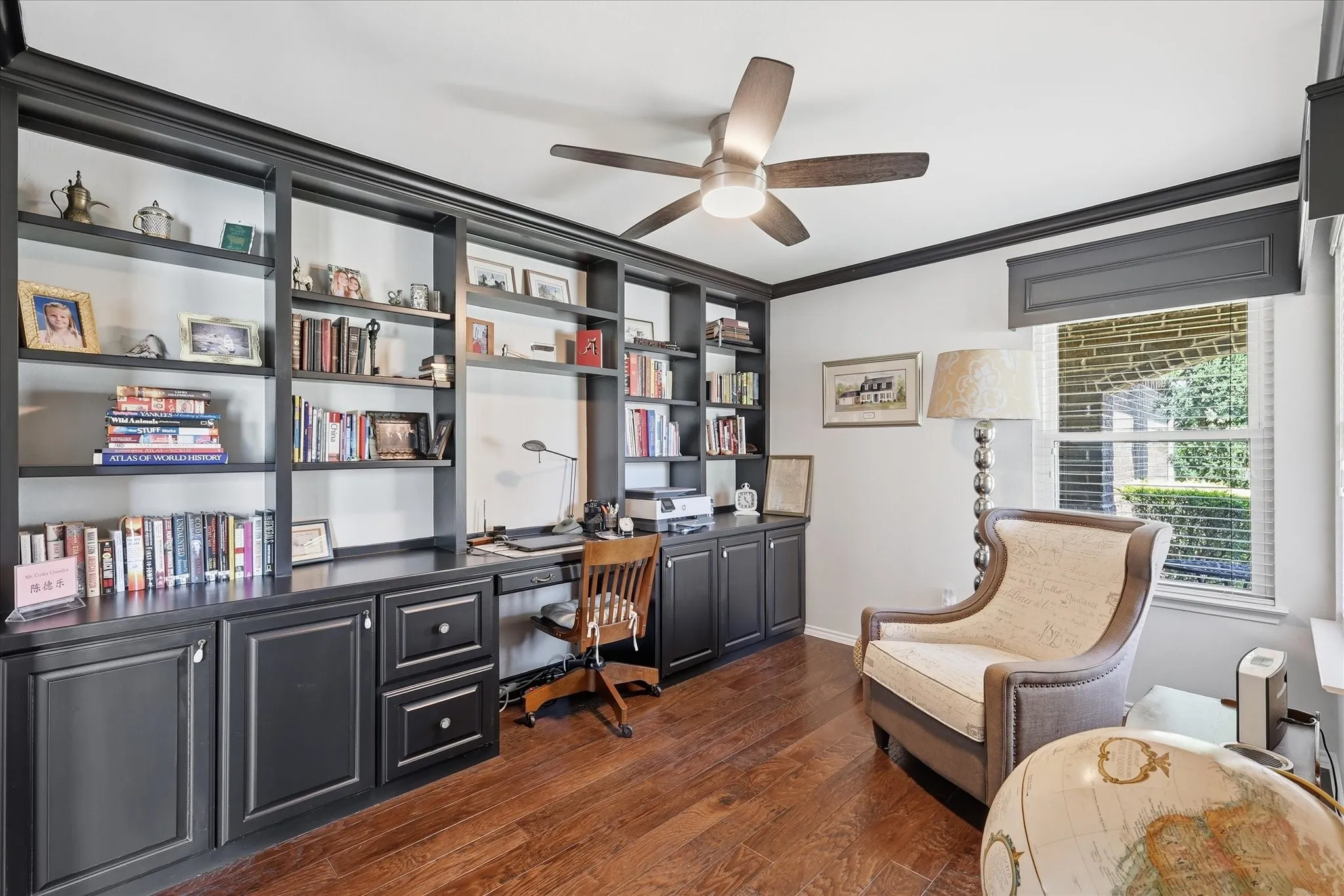 Dedicated office space featuring extensive built-in cabinetry and shelving, integrated desk, wood-finish flooring, and a ceiling fan