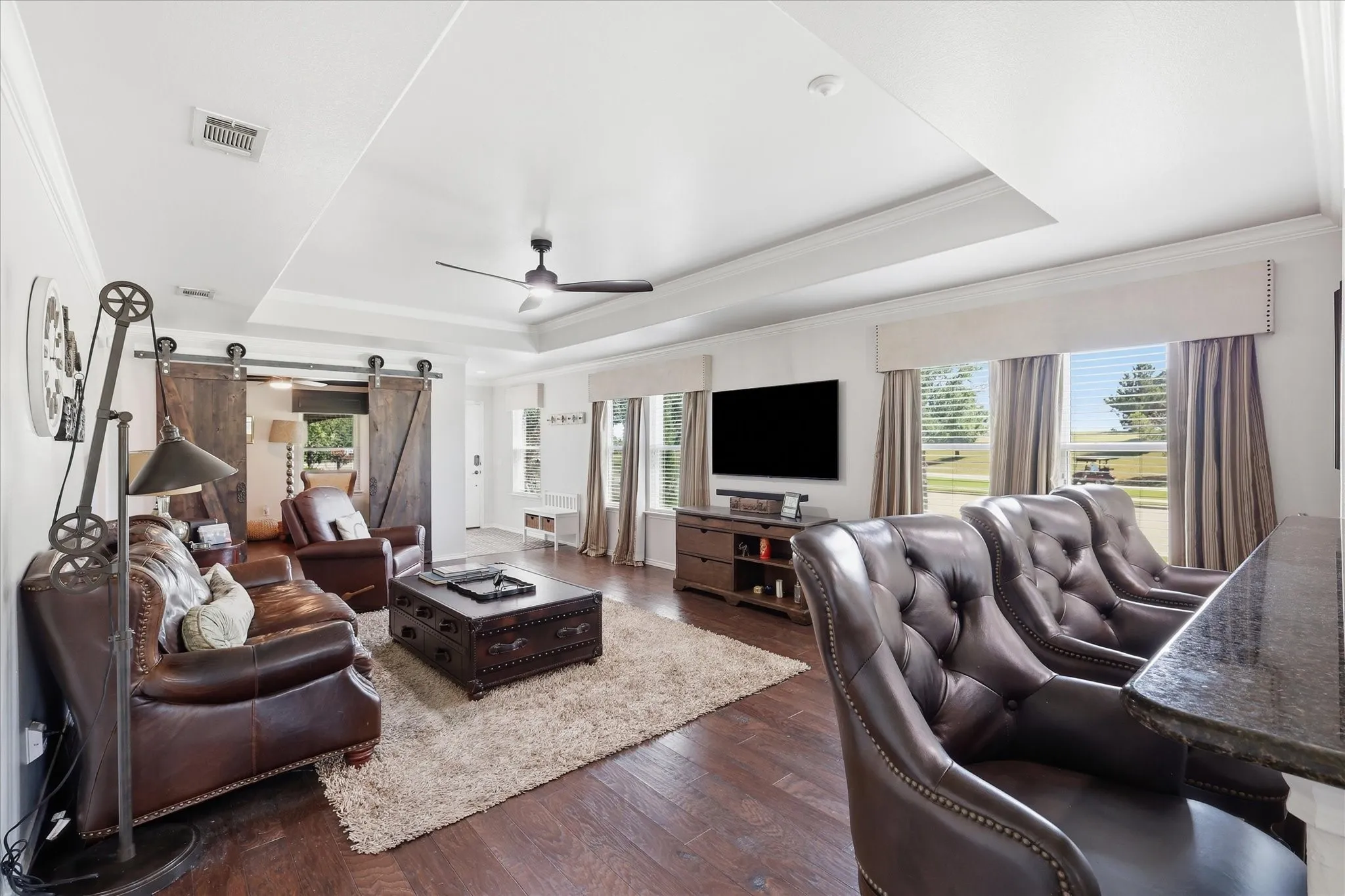 Spacious living area featuring wood-finish flooring, a tray ceiling, and a ceiling fan