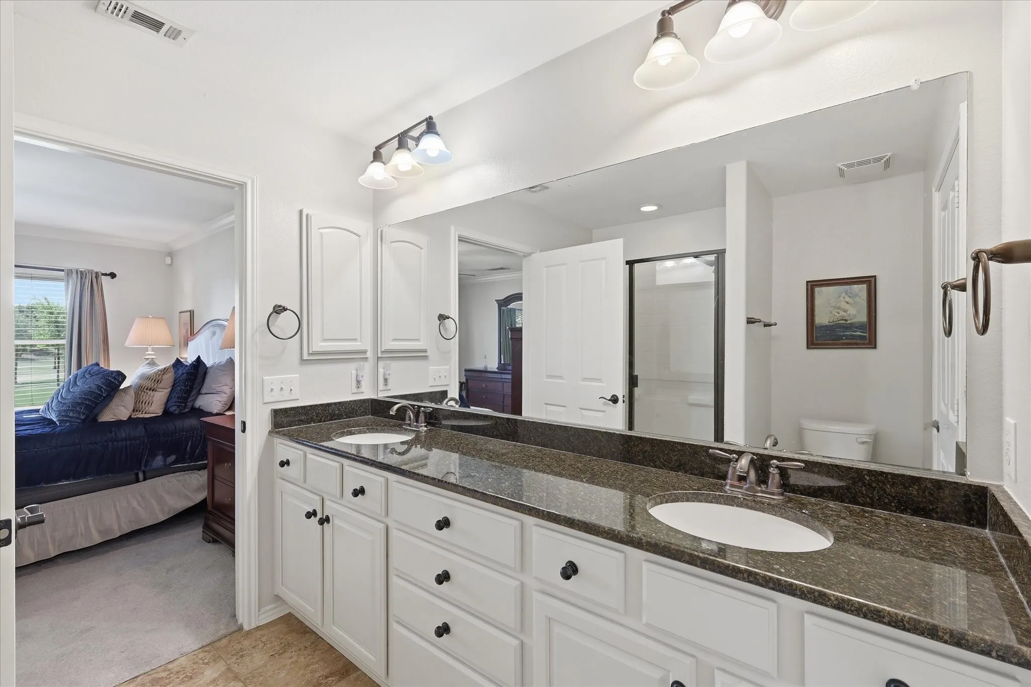 Primary Bathroom with Dual vanity with dark granite countertops and white cabinetry