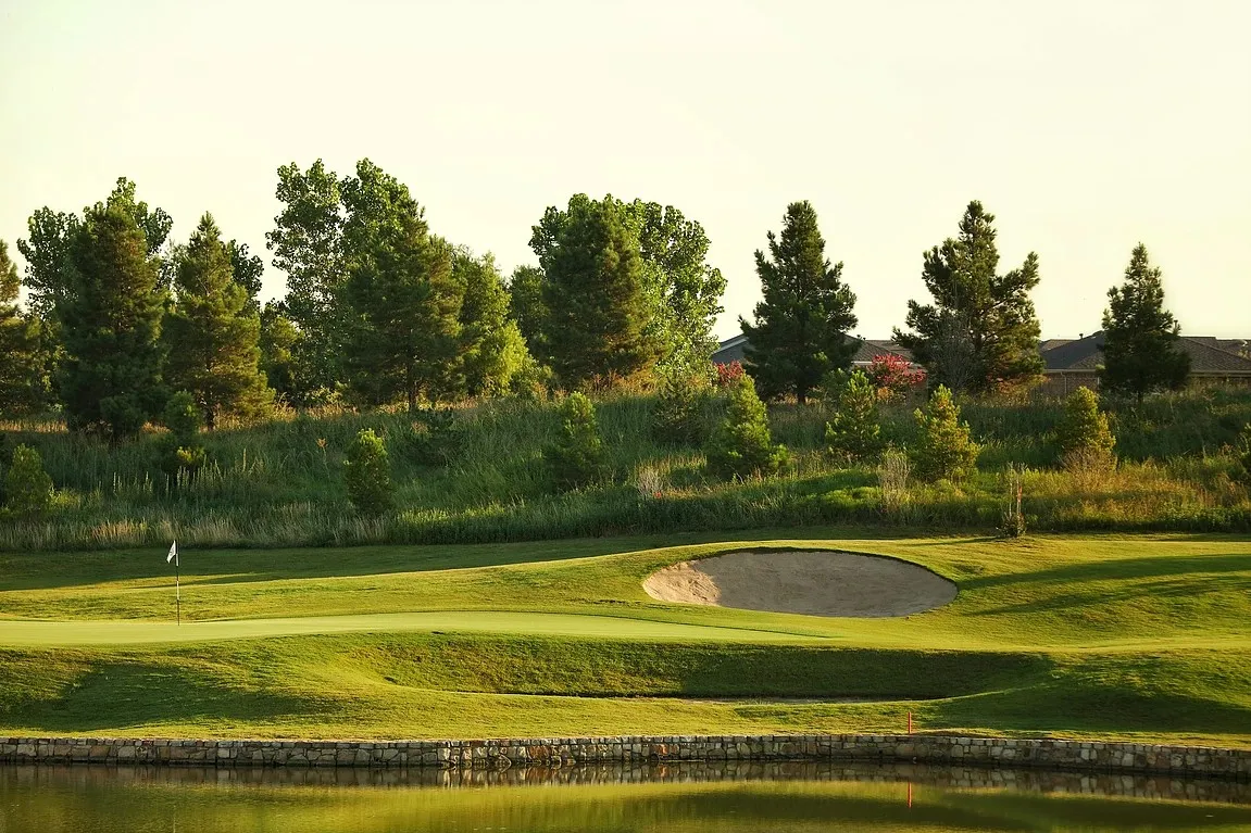 Frisco Lakes Golf course setting featuring a manicured green with a flag, sand bunker, and a surrounding water feature with a stone retaining wall
