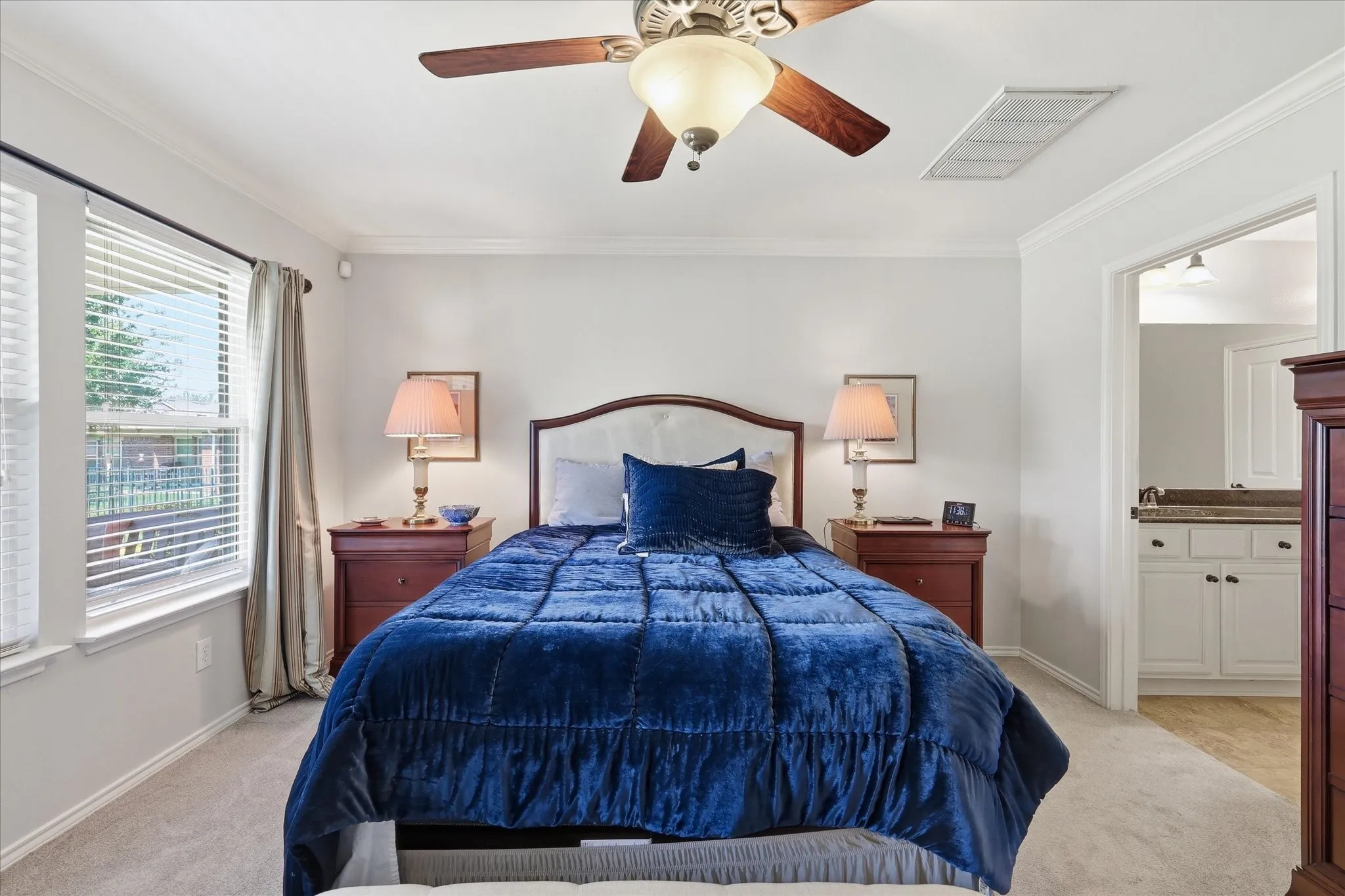 Carpeted bedroom featuring a ceiling fan with integrated lighting, crown molding, and dual windows with blinds and Ensuite Bathroom