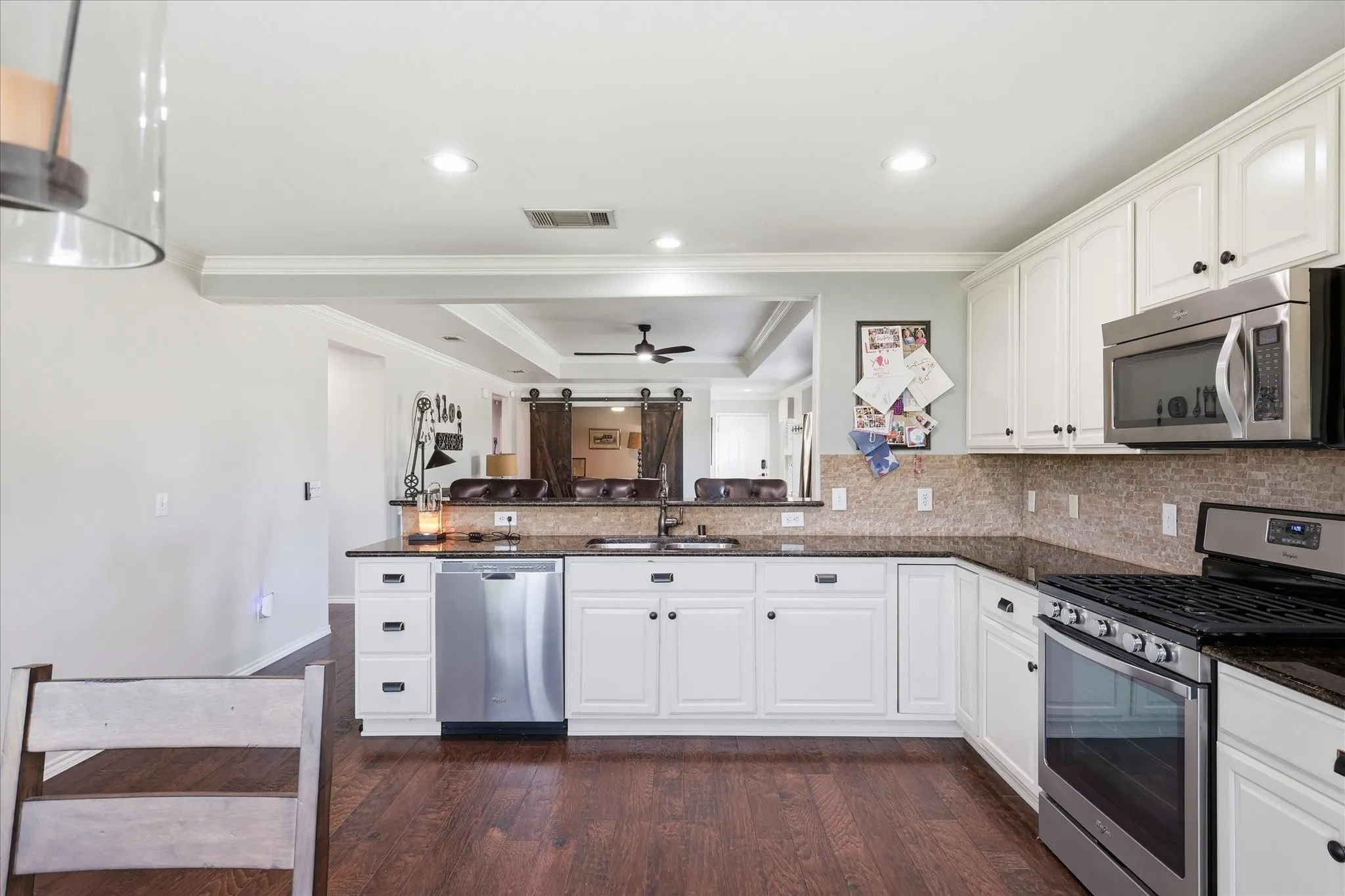 Kitchen featuring white cabinetry, dark stone countertops, stainless steel appliances, a tile backsplash, and wood-finish flooring