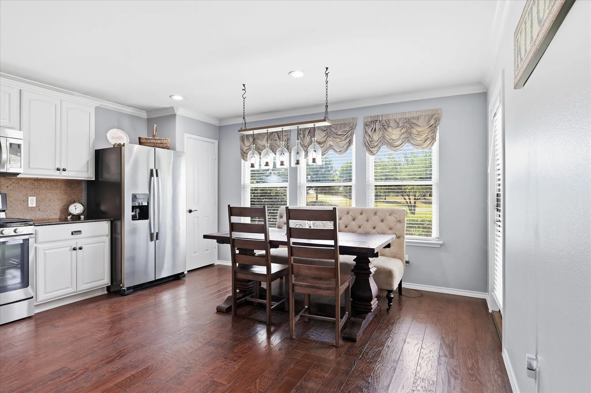 Kitchen and dining area featuring wood-finish flooring, white cabinetry, stainless steel appliances, and a trio of windows