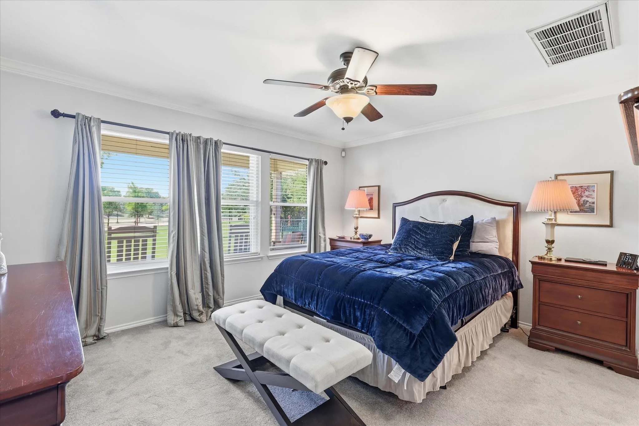 Bedroom featuring triple windows with blinds and curtains, a ceiling fan with integrated lighting, crown molding, and light-colored carpeting