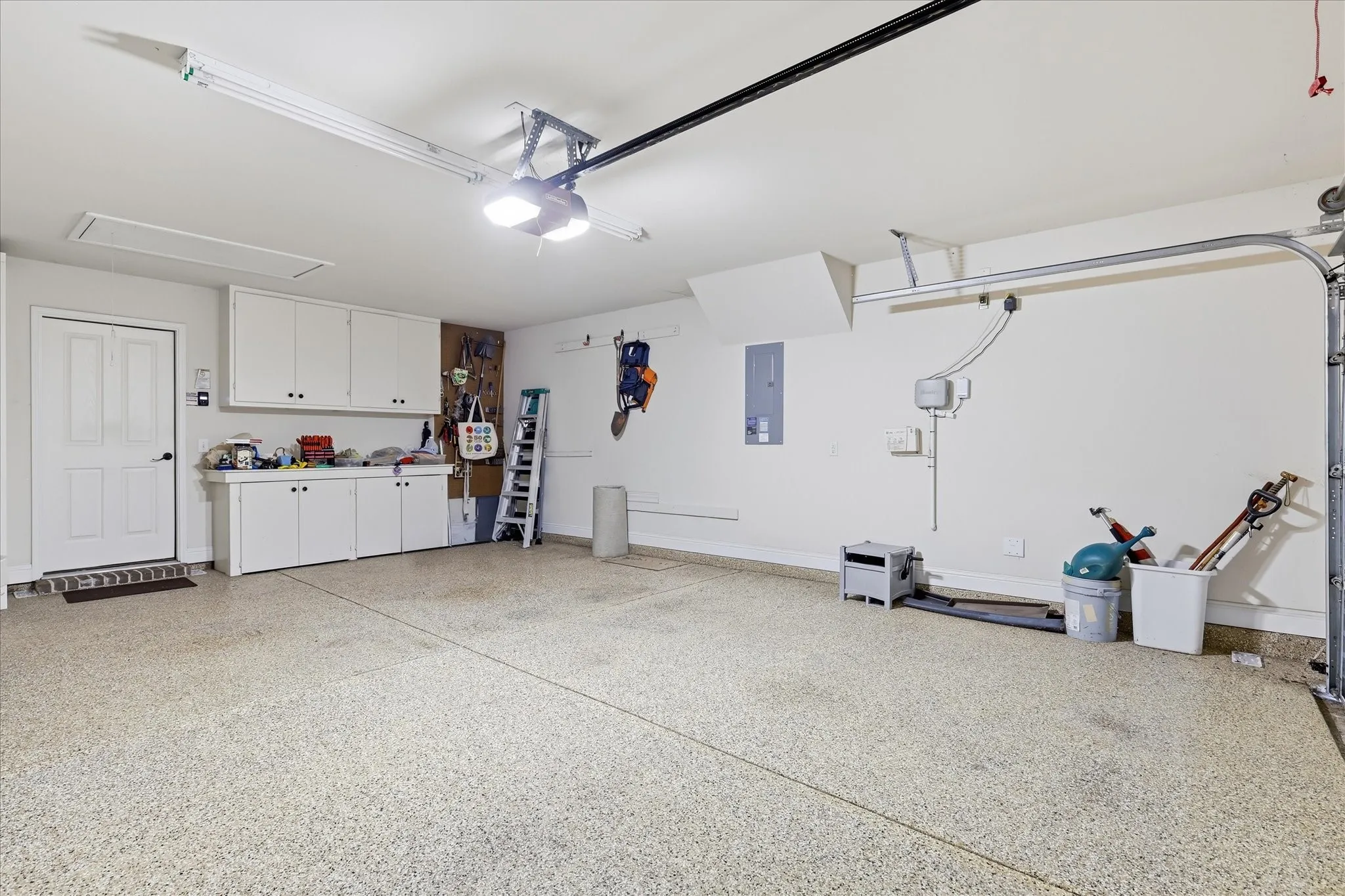 Spacious garage featuring a durable speckled epoxy floor, built-in white cabinetry, a dedicated workbench area, ample overhead lighting, and an automatic garage door opener