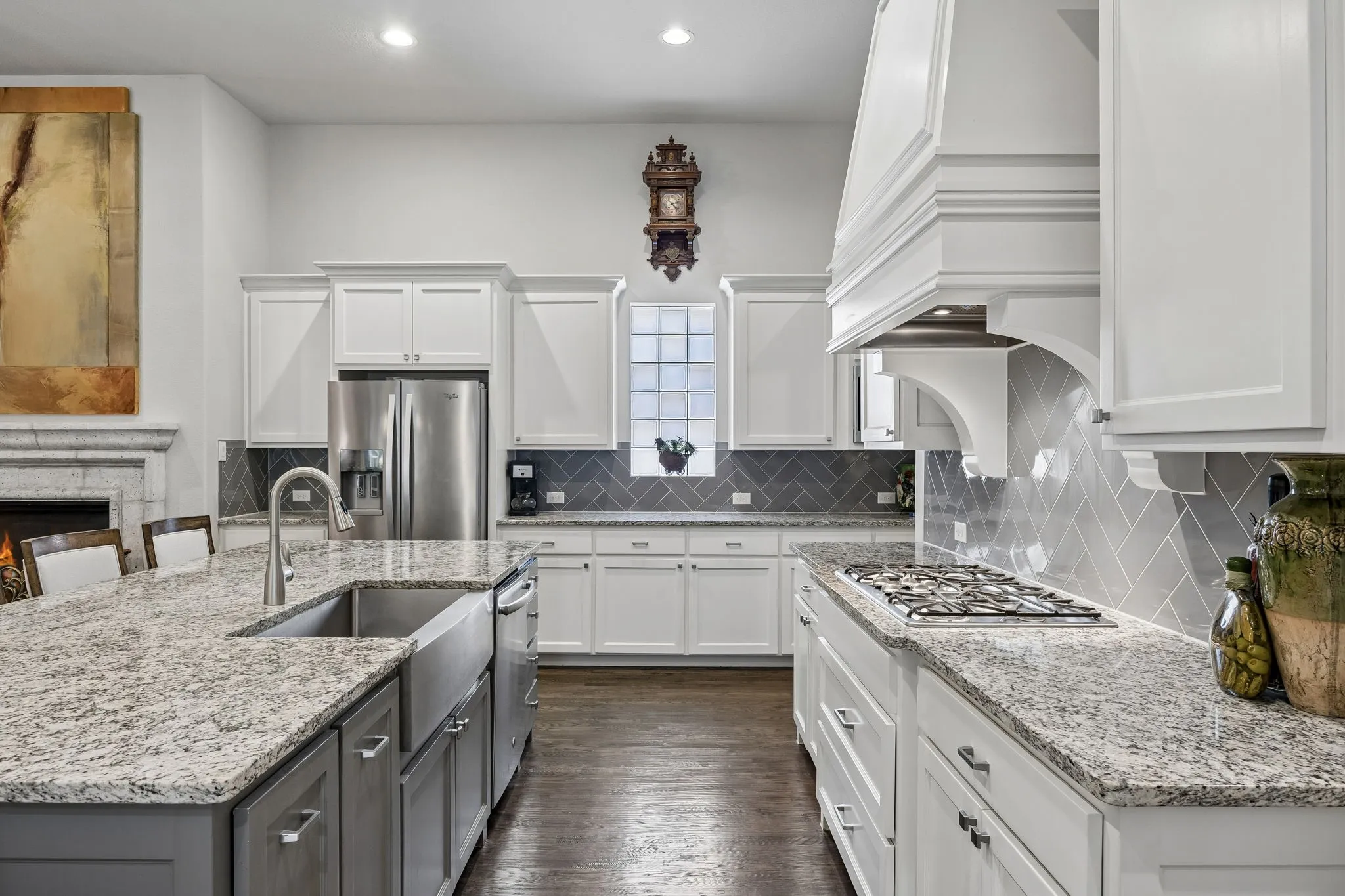 Oversized island with natural stone, farm sink, numerous cabinets, gas cooktop and vent hood.