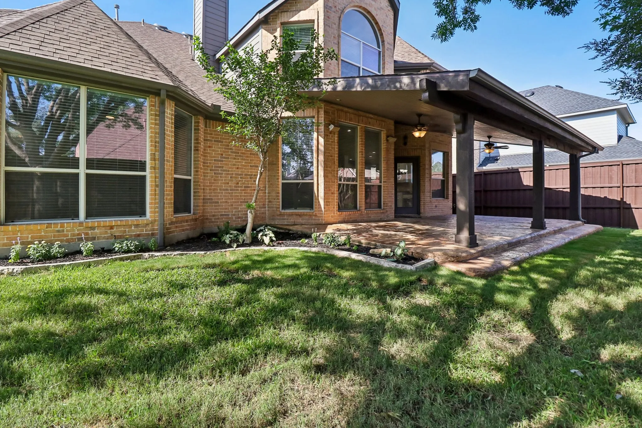 Expansive covered patio featuring two ceiling fans, recessed lighting, and a patterned stone-look surface