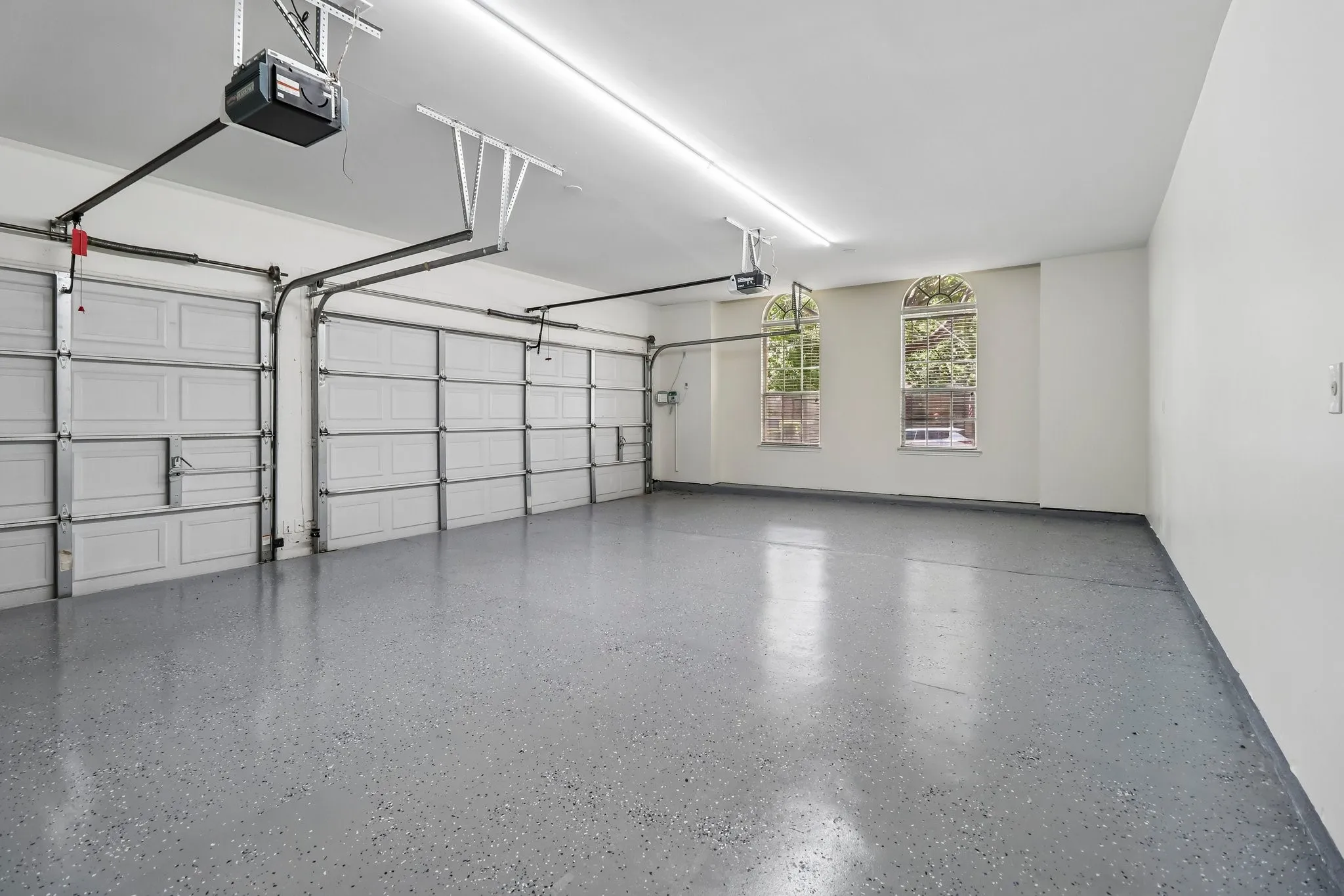Three car garage featuring a speckled epoxy floor coating, two arched windows, a white ceiling with LED lighting, and two individual garage doors with automatic openers.