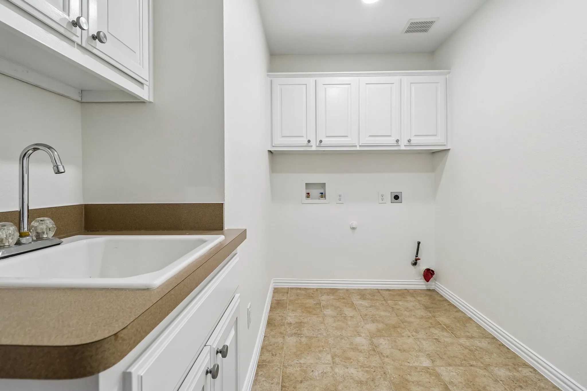 Utility room featuring a built-in sink, upper cabinets, tile flooring, new water valves and option for gas or electric dryer.