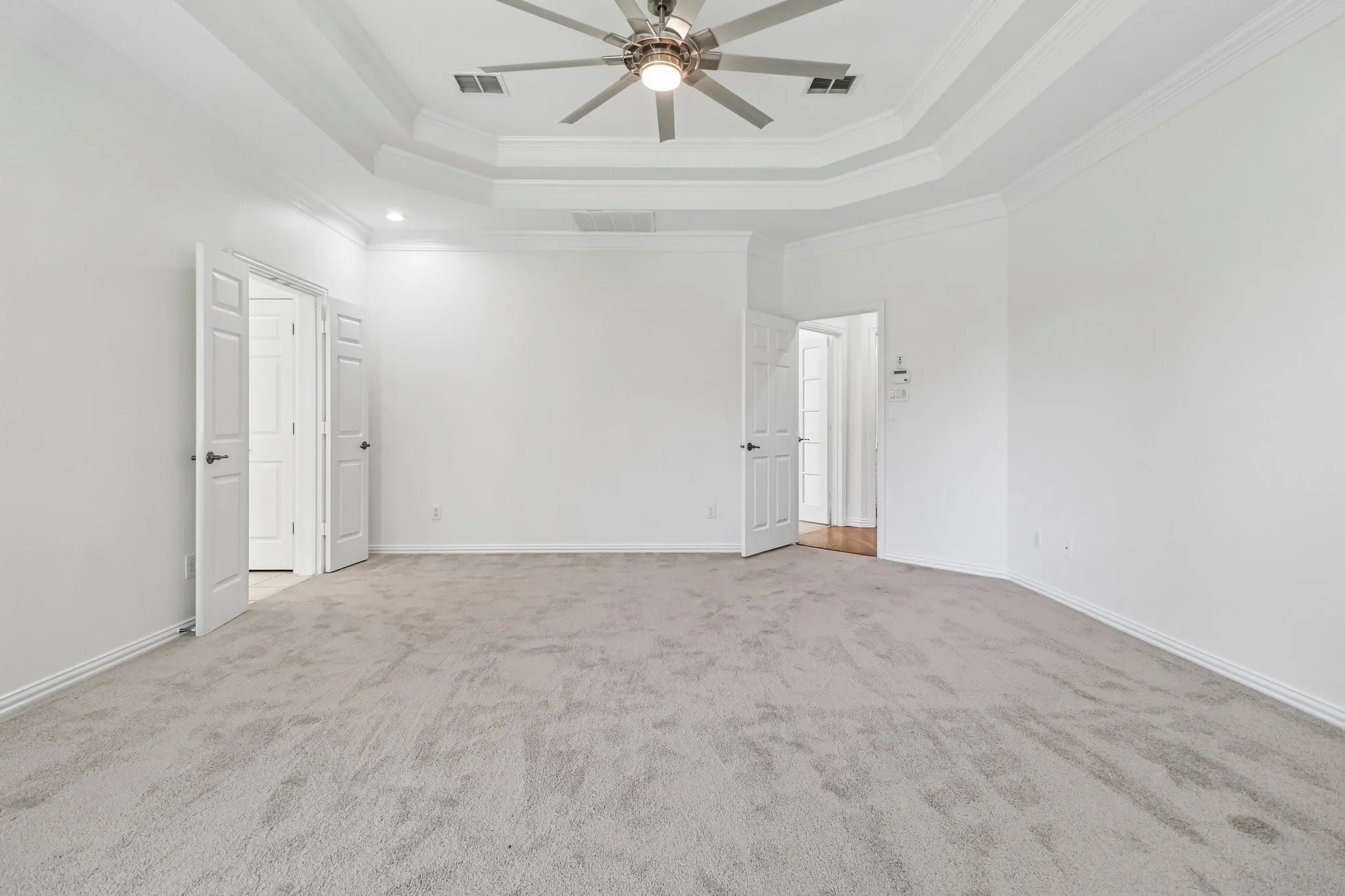 Expansive primary bedroom featuring a multi tray ceiling, double staged crown molding, 72" ceiling fan with integrated lighting, and new light-toned carpet flooring