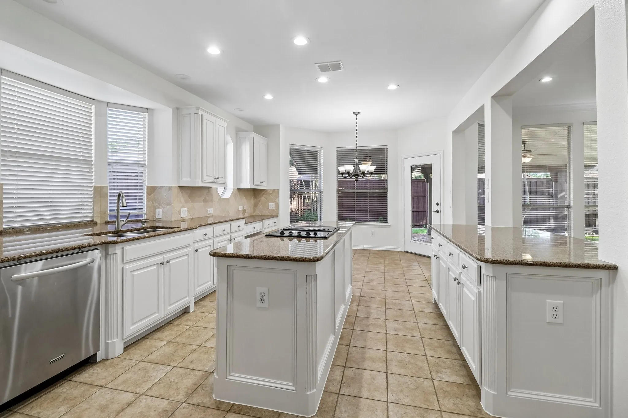 Modern kitchen featuring a central island with down draft cook top, white cabinetry, integrated stainless steel appliances, granite counter tops and tile flooring.