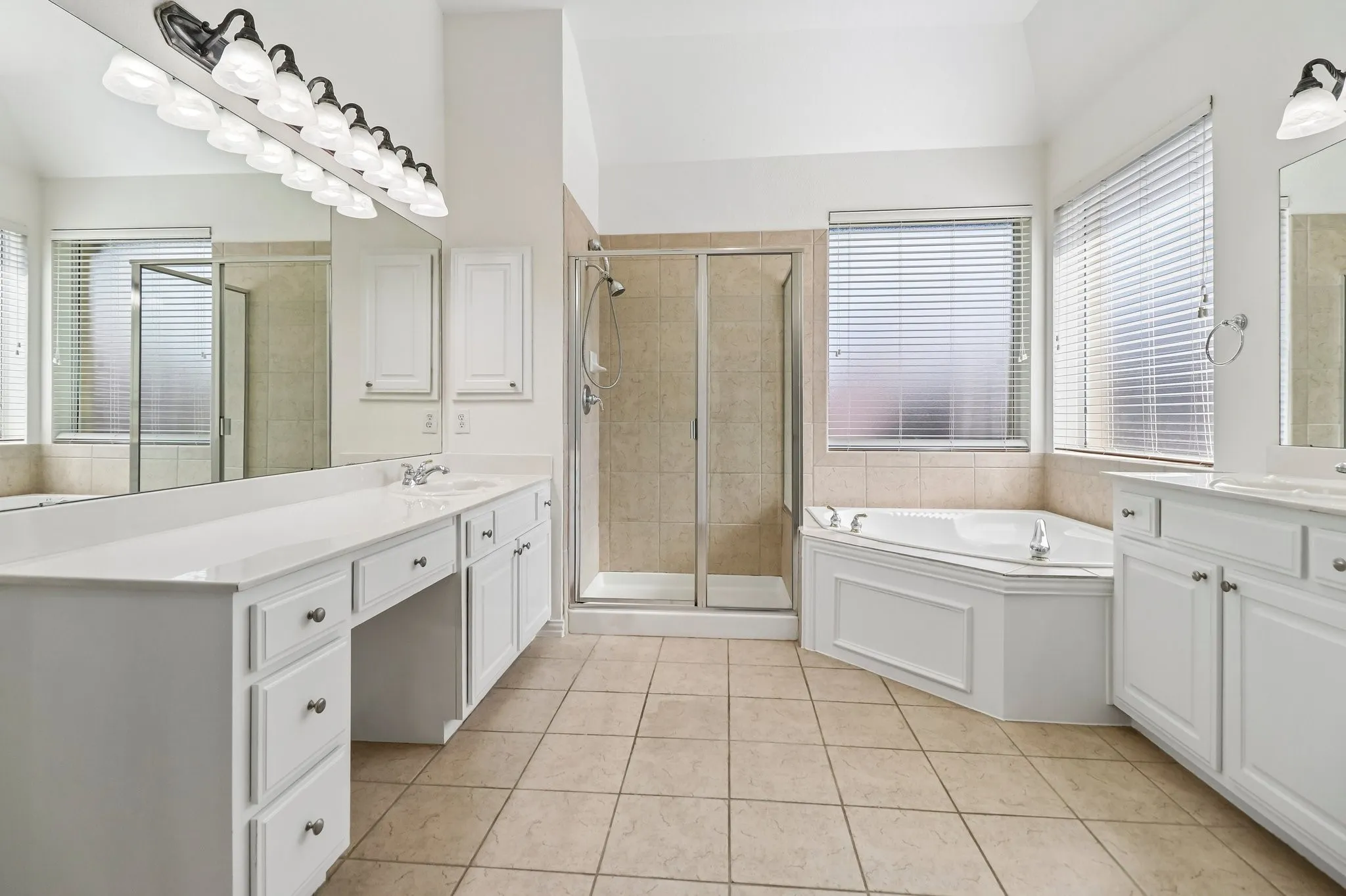 Spacious bathroom featuring a dual vanity with white cabinetry, a walk-in shower with tile surround, a corner jetted soaking tub, and tile flooring.