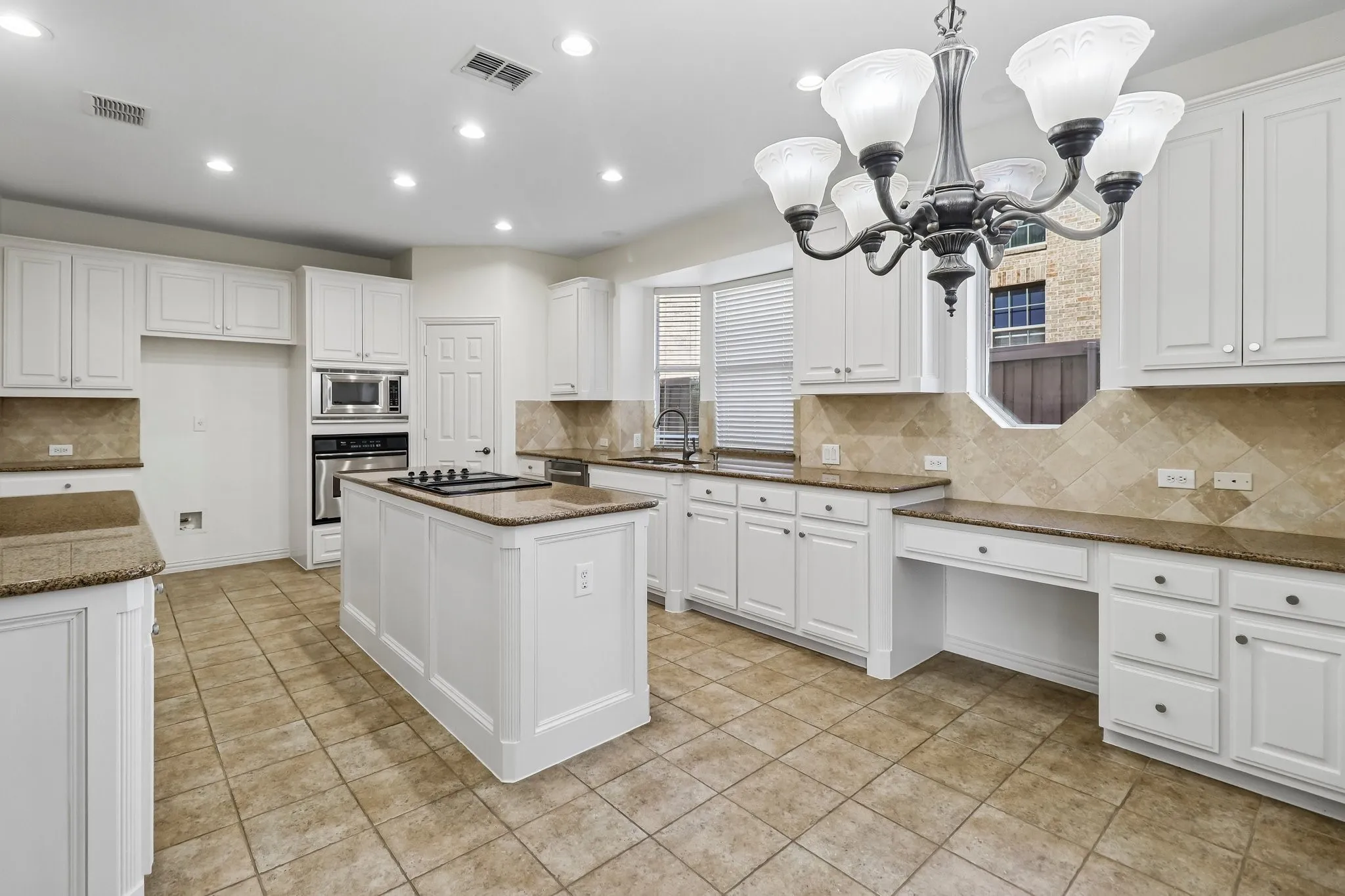 Kitchen featuring white cabinetry, granite countertops, a central island with a built-in cooktop, tile flooring, and a tile backsplash