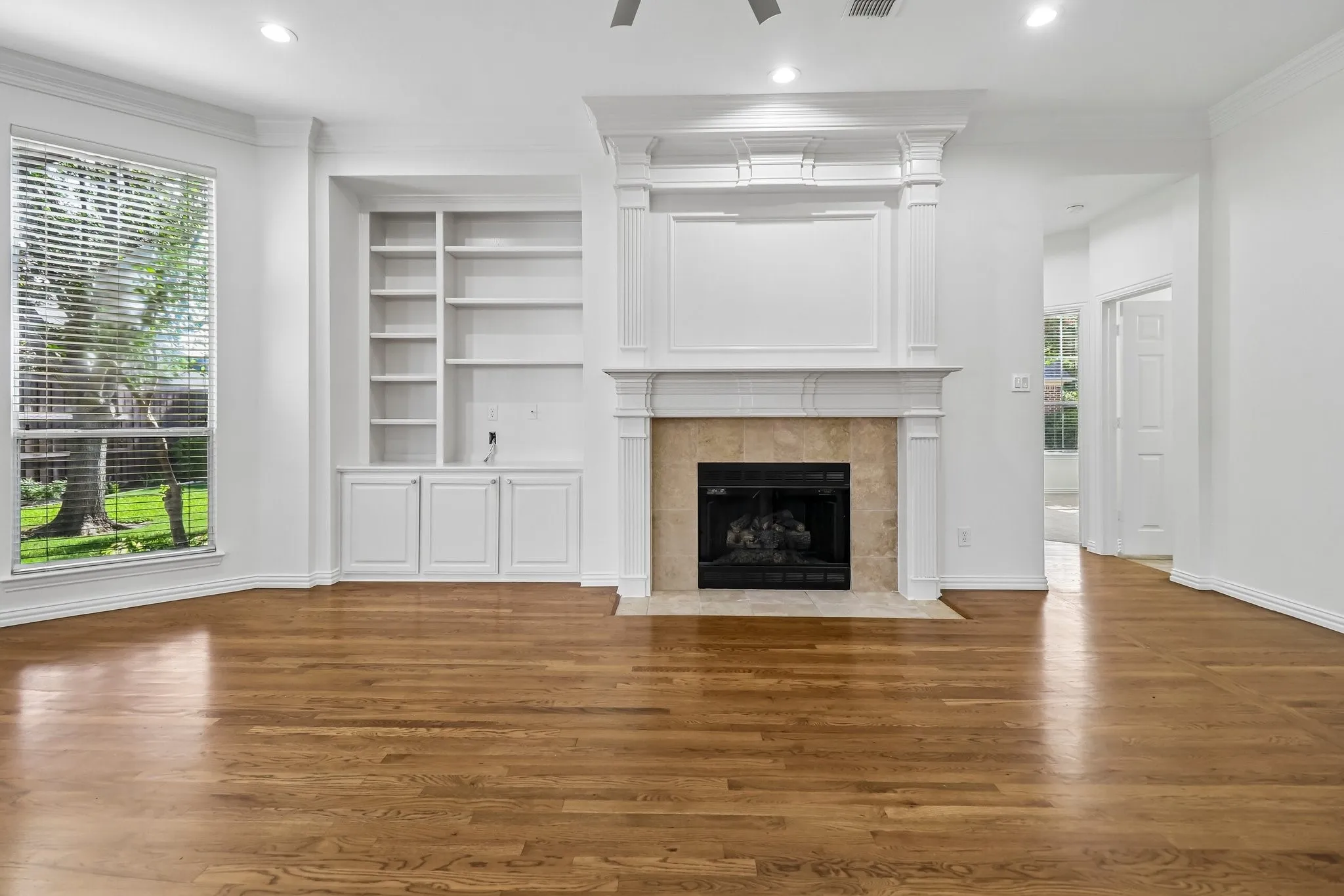 Living space featuring hardwood floors, a decorative double staged fireplace with gas logs built-in shelving, 72" ceiling fan and plenty of LED can lights.