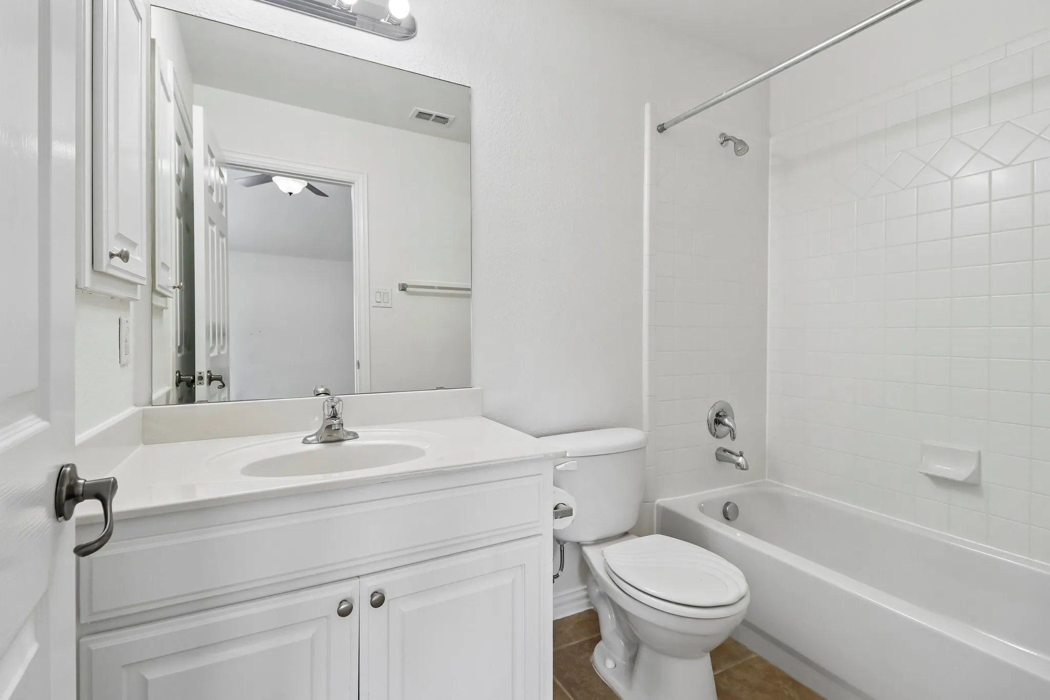 Full bathroom featuring a white vanity with a built-in sink, chrome fixtures, and a white tiled shower-tub combination.