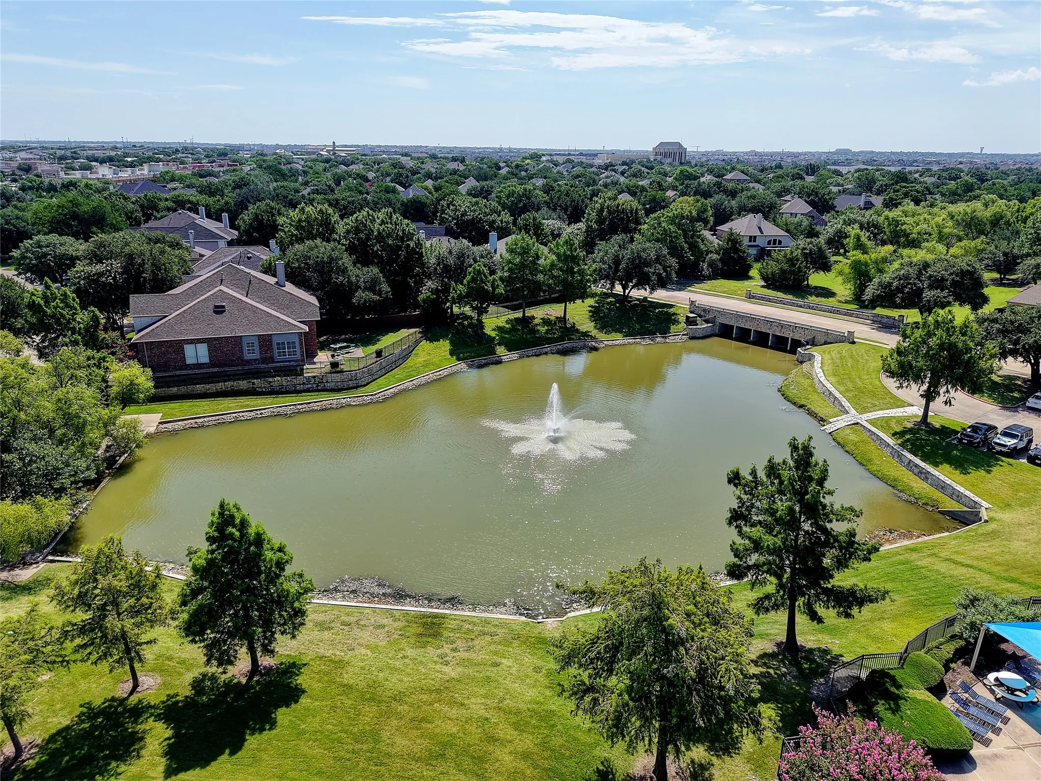Pond with a central fountain, bordered by a stone retaining wall and expansive green lawns