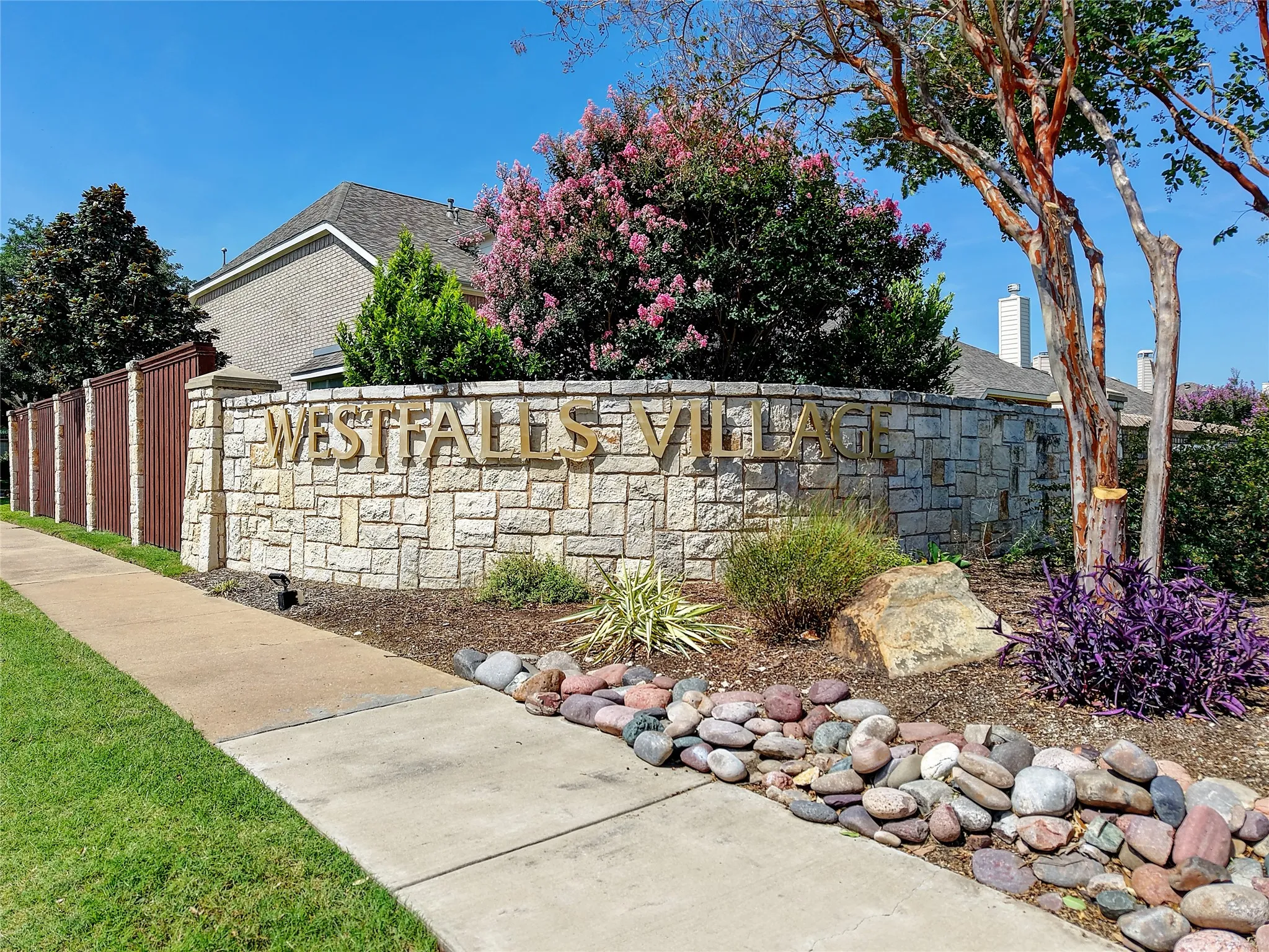 Stone entry monument featuring dimensional lettering, surrounded by varied landscaping with mature shrubs and flowering trees