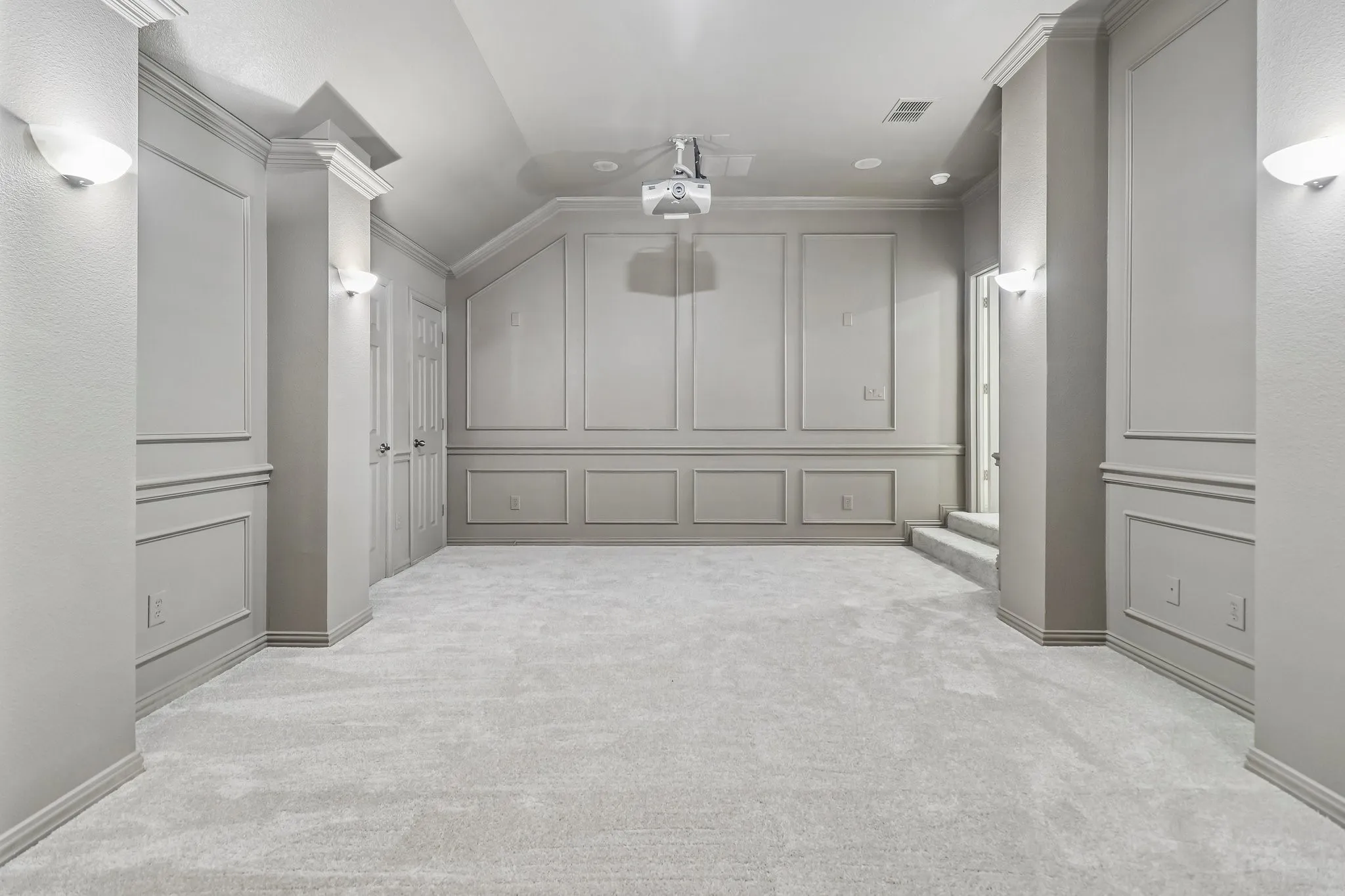 Carpeted media room featuring wainscoting, vaulted ceiling, wall sconces, crown molding and a ceiling-mounted projector