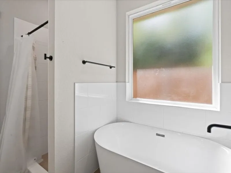 Freestanding soaking tub with a matte black wall-mounted faucet, complemented by a white tiled wall surround and a frosted window