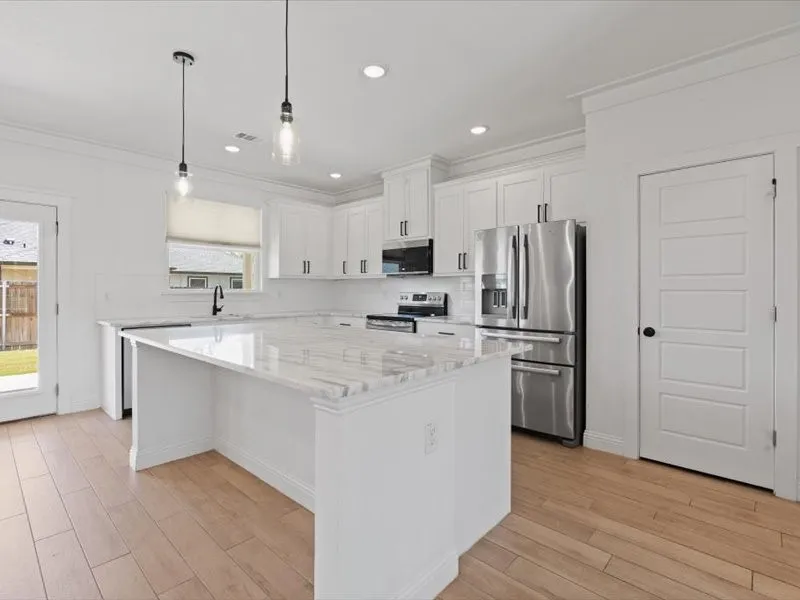 Modern kitchen featuring an expansive center island with a stone countertop, white shaker cabinetry, stainless steel appliances, and wood-finish flooring