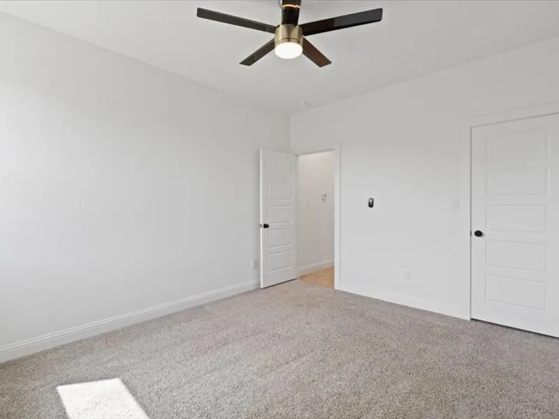 Spacious room featuring light gray carpet, white baseboards, and a modern ceiling fan with integrated lighting