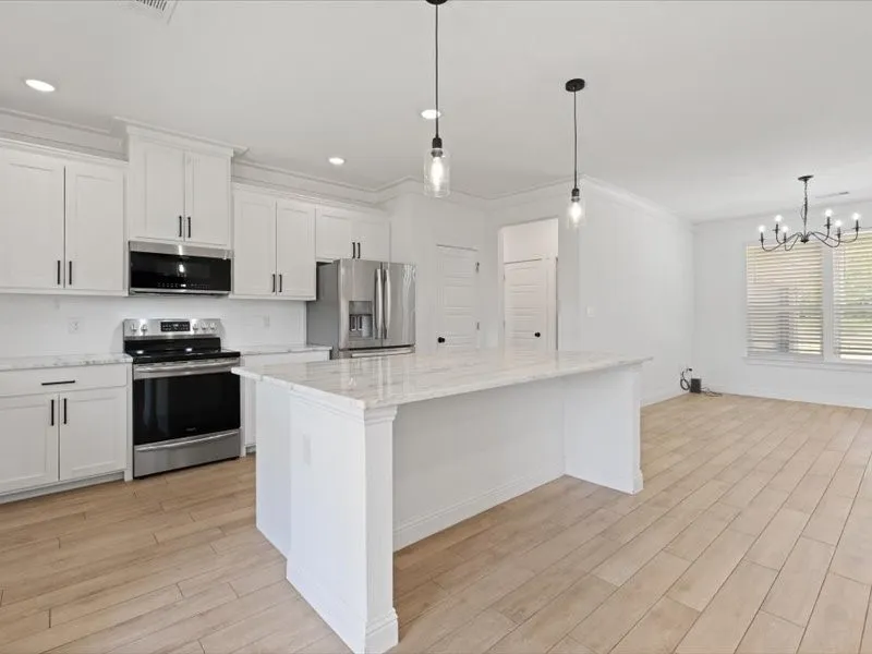 Open concept kitchen featuring an island with a light-toned countertop, white cabinetry with dark hardware, stainless steel appliances, and wood-finish flooring