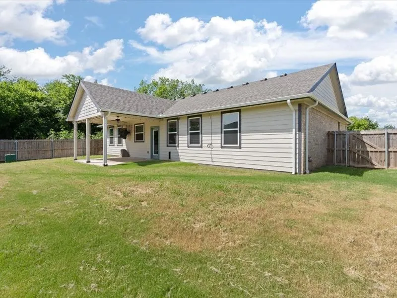 Expansive backyard featuring a covered patio, ceiling fan, and privacy fencing