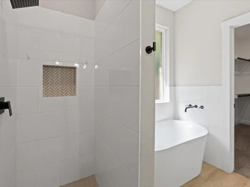 Shower with white subway tile surround and a herringbone-patterned tile niche, complemented by a freestanding soaking tub with wall-mounted matte black fixtures