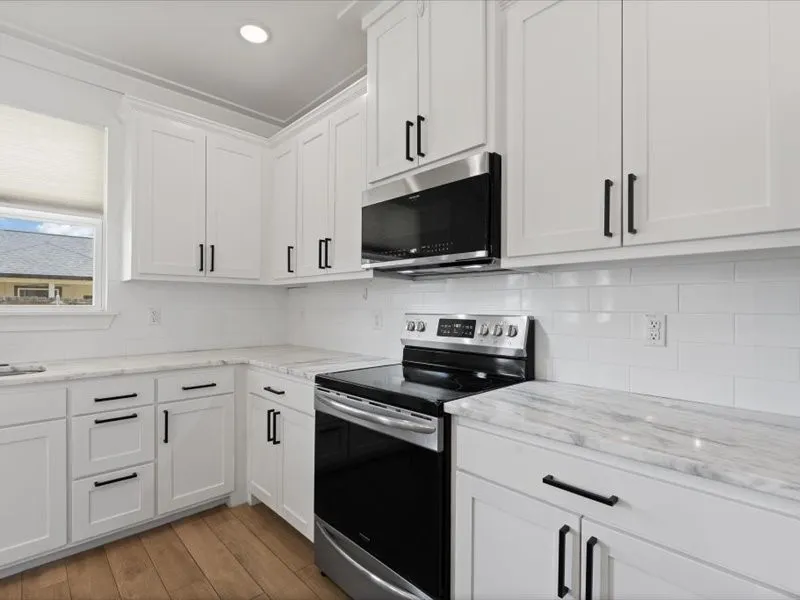 Kitchen featuring white cabinetry with matte black hardware, stone countertops with subtle veining, a white subway tile backsplash, stainless steel appliances, and wood-finish flooring