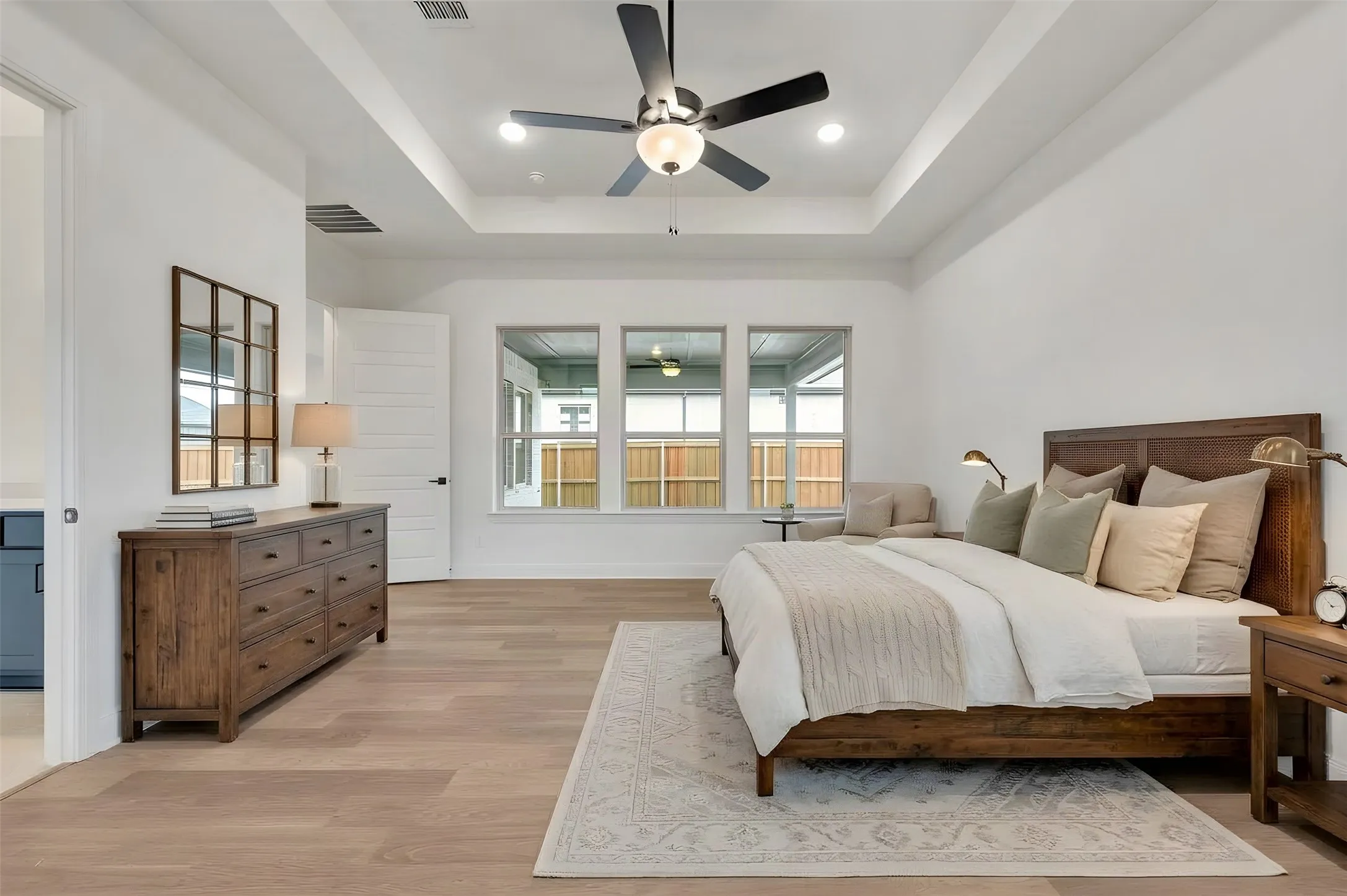 Tray ceiling with a ceiling fan and recessed lighting, light wood-finish flooring, and multiple windows