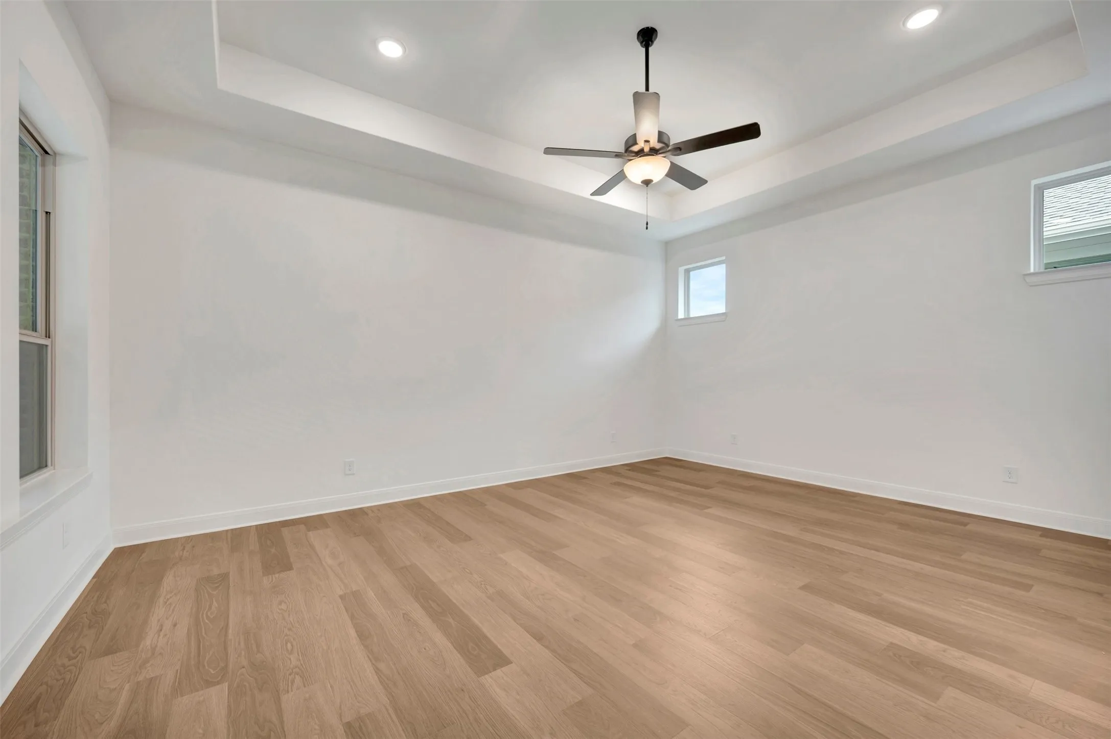 Recessed tray ceiling with integrated lighting, wood-finish flooring, and ceiling fan