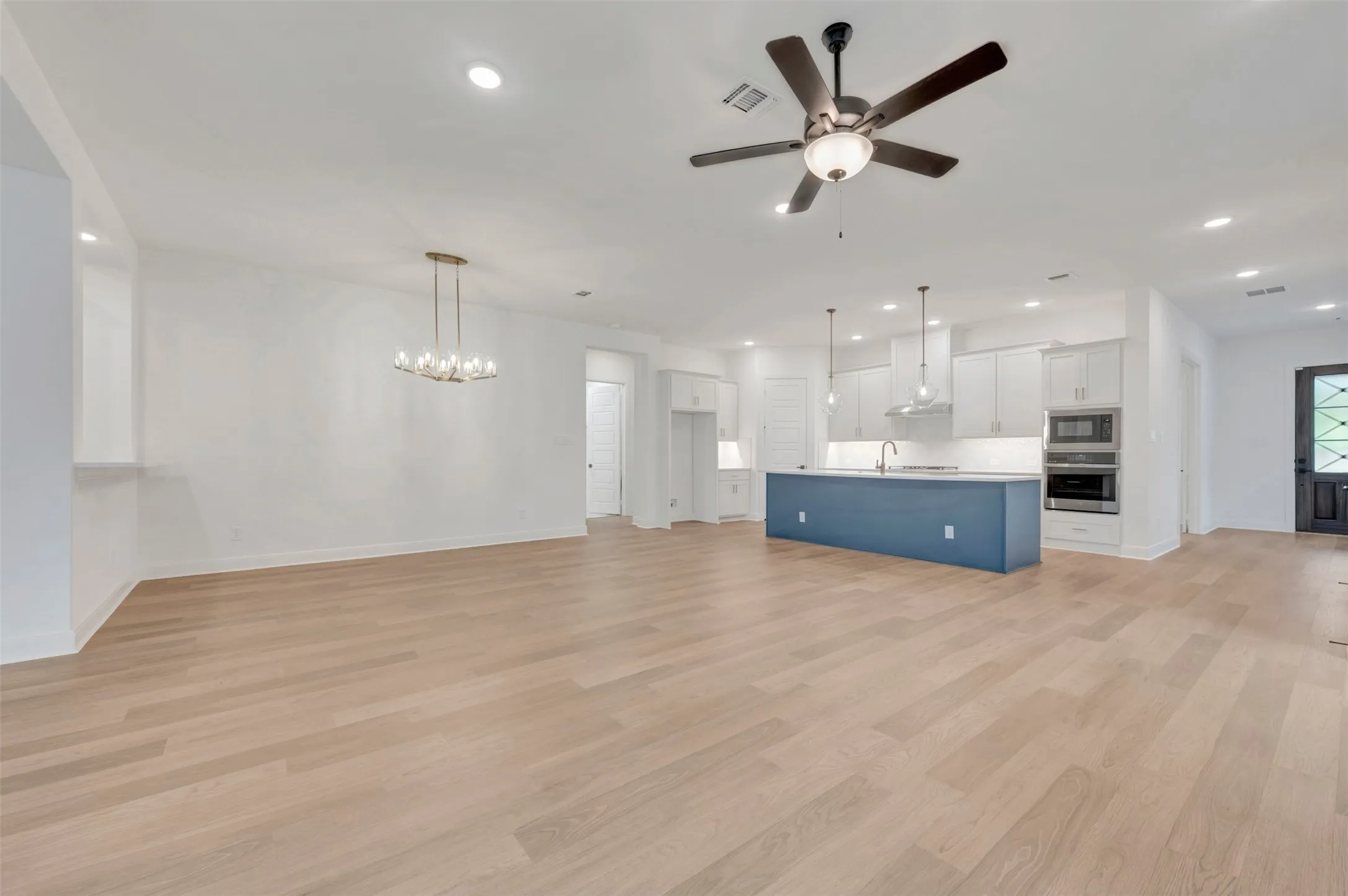 Wood-finish flooring throughout, modern kitchen with white cabinetry, stainless steel appliances, blue island, and recessed lighting