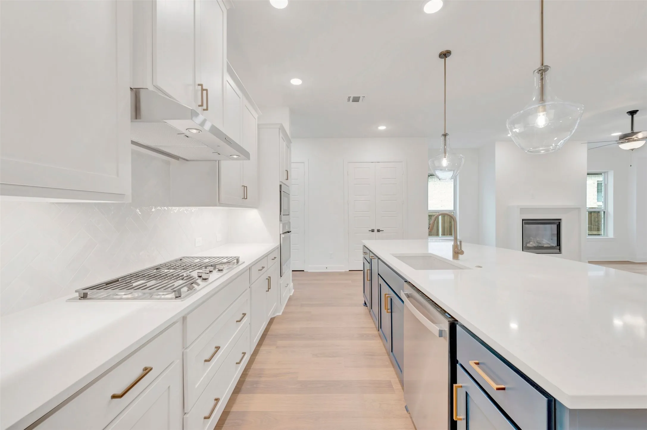 Spacious kitchen featuring white cabinetry, a gas cooktop, herringbone tile backsplash, and a large island with an integrated sink and pendant lighting