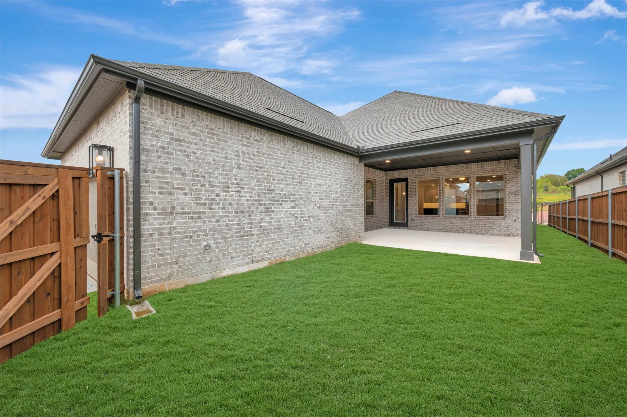 Expansive grassy yard area with a covered patio, brick exterior, and a wood fence