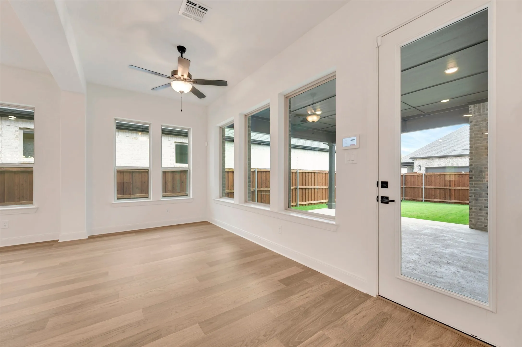 Wood-finish flooring, multiple large windows, ceiling fan, full-light door, and a covered patio