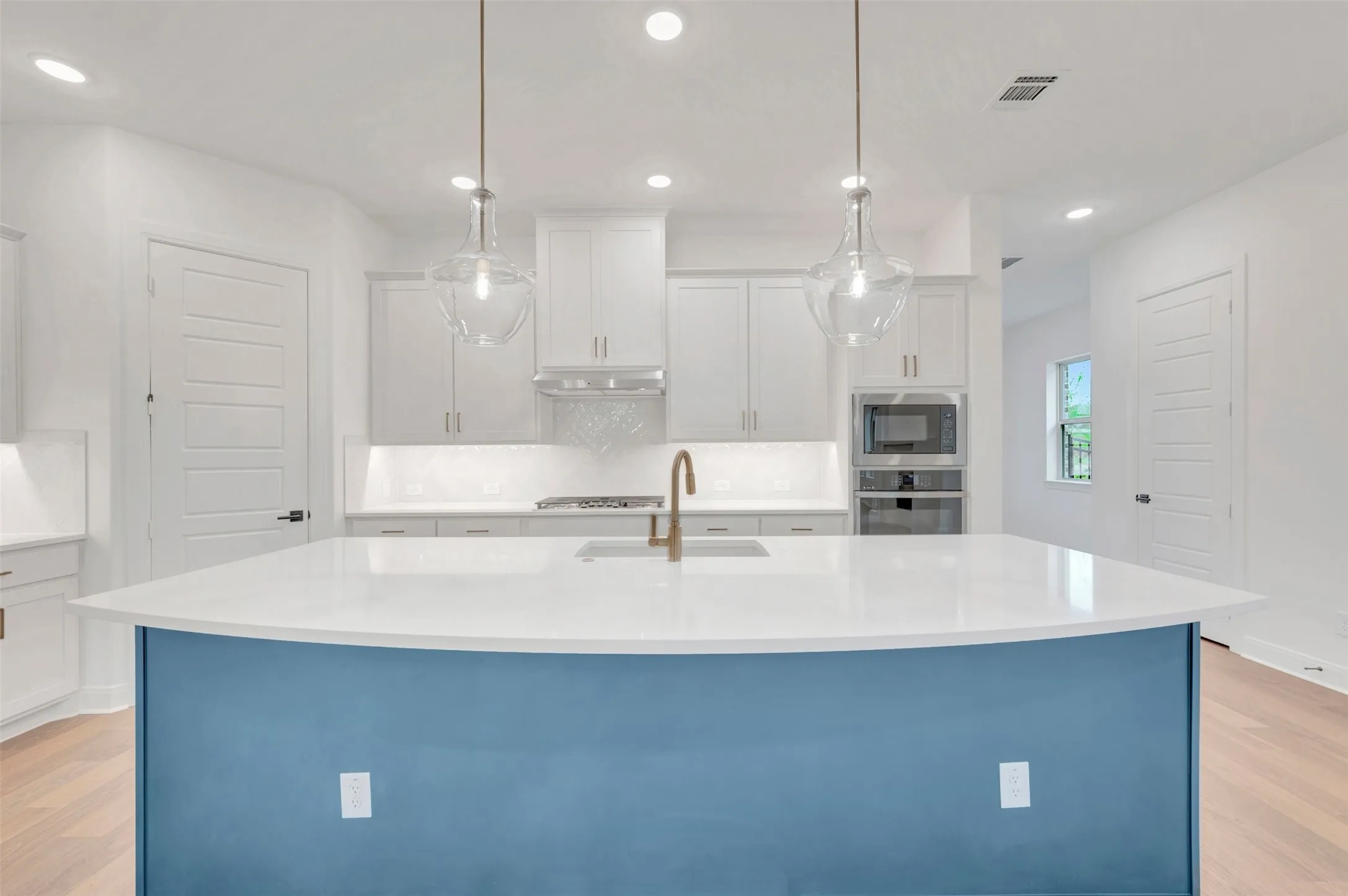 Kitchen featuring a curved island with a white countertop and blue-painted base, white cabinetry, stainless steel appliances, and two glass pendant lights