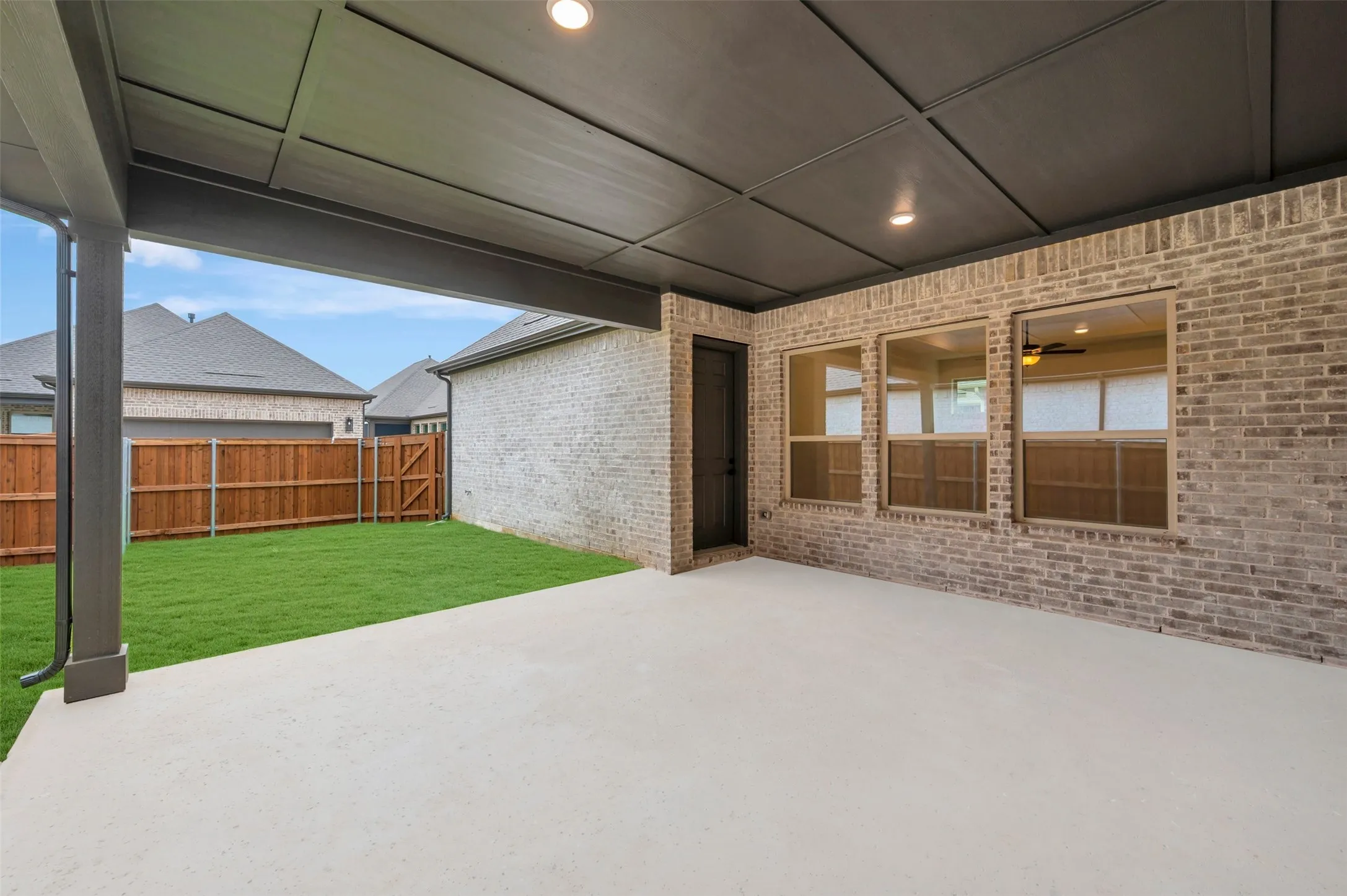 Covered patio with a concrete surface, brick exterior, ceiling lighting, and a fenced backyard