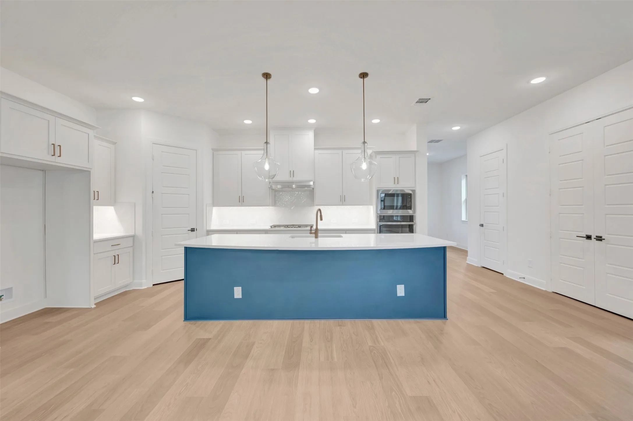 Kitchen featuring a central island with a blue base, white countertops, and a brass-finish faucet