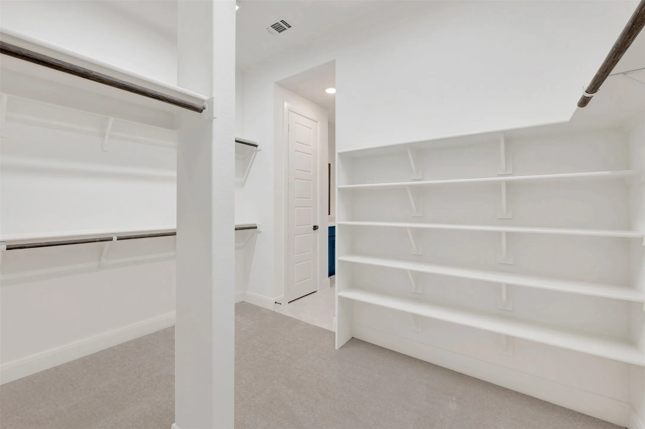 Spacious walk-in closet featuring light-toned carpeting and extensive built-in shelving, complemented by multiple hanging rods for organization