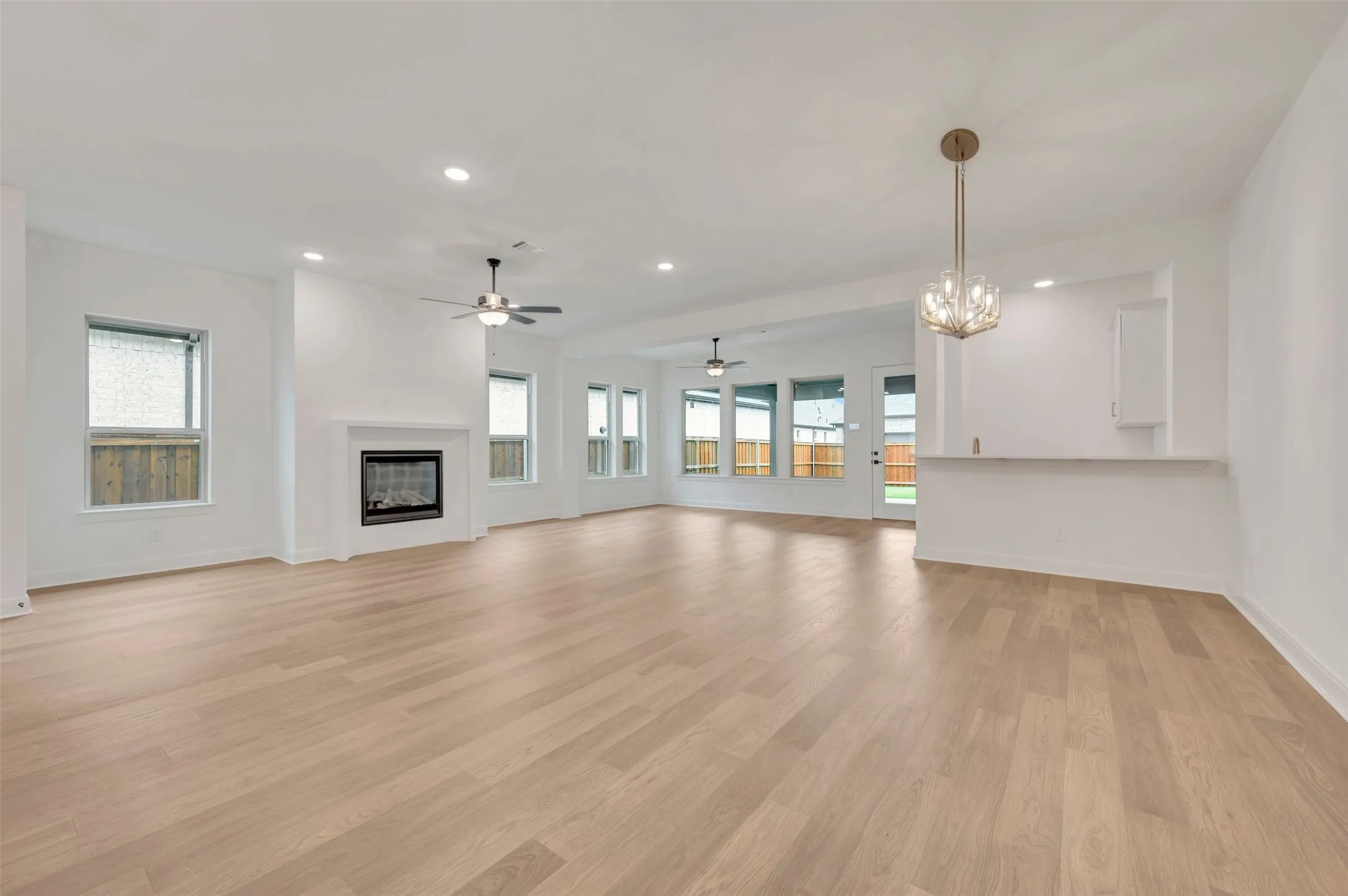 Open-concept living area featuring wood-finish flooring, a fireplace with a mantel, recessed lighting, and a contemporary chandelier
